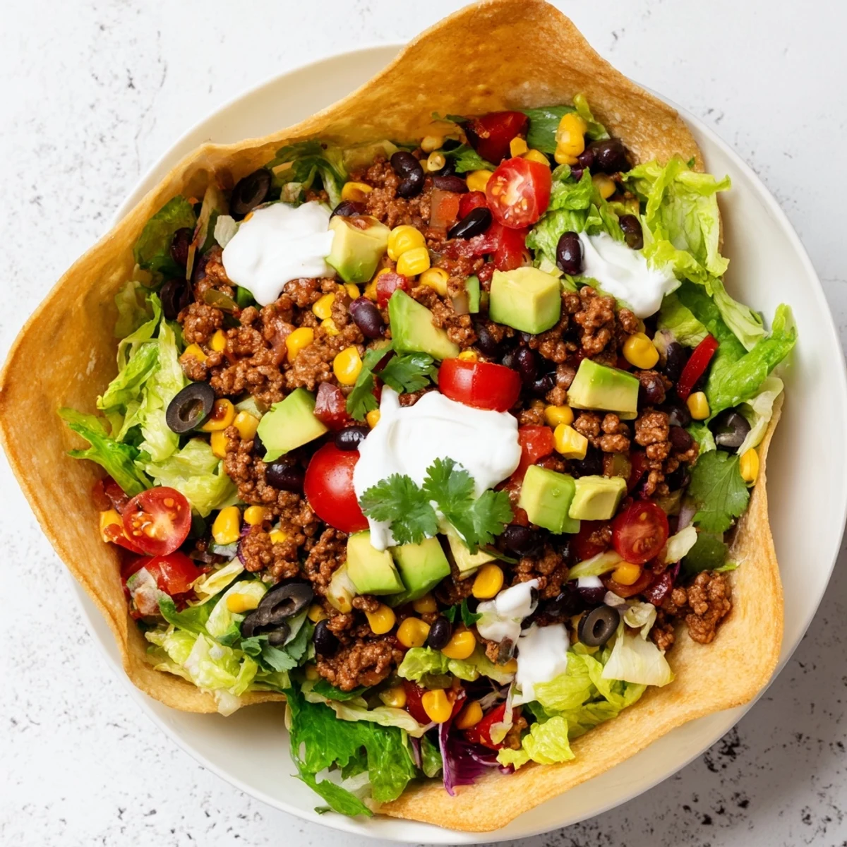A close-up of a Beef Taco Salad in Tortilla Bowl, overflowing with colorful fresh ingredients and cheese.