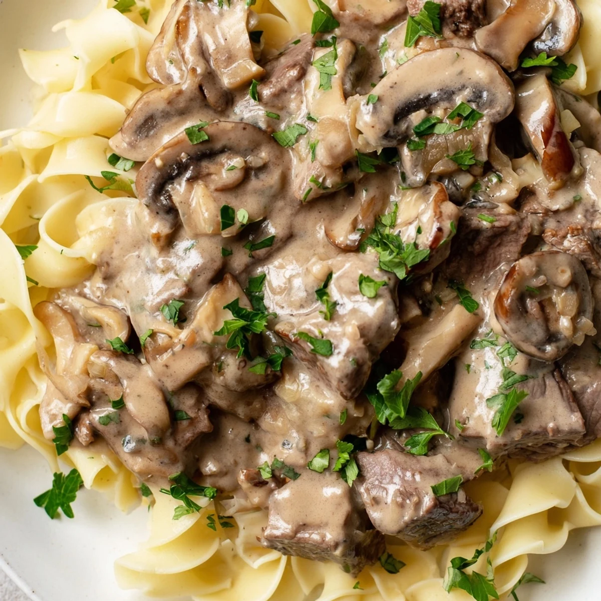 Creamy beef stroganoff with tender beef and mushrooms served over wide egg noodles, garnished with fresh parsley.