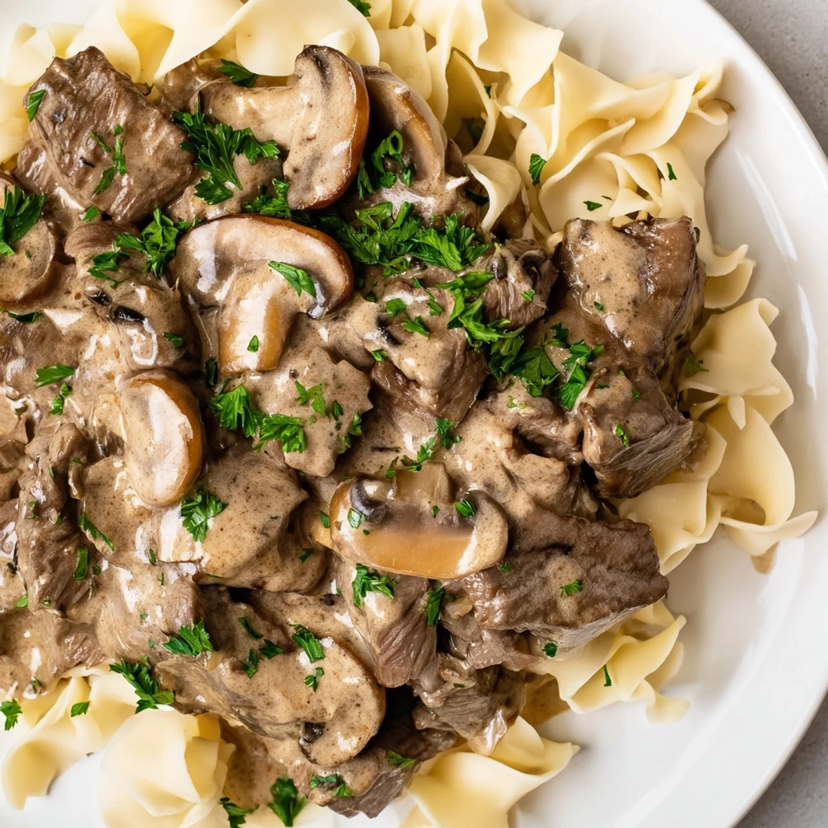 Homestyle Russian-American beef stroganoff served over egg noodles, garnished with parsley, paired with green beans for a comforting meal.
