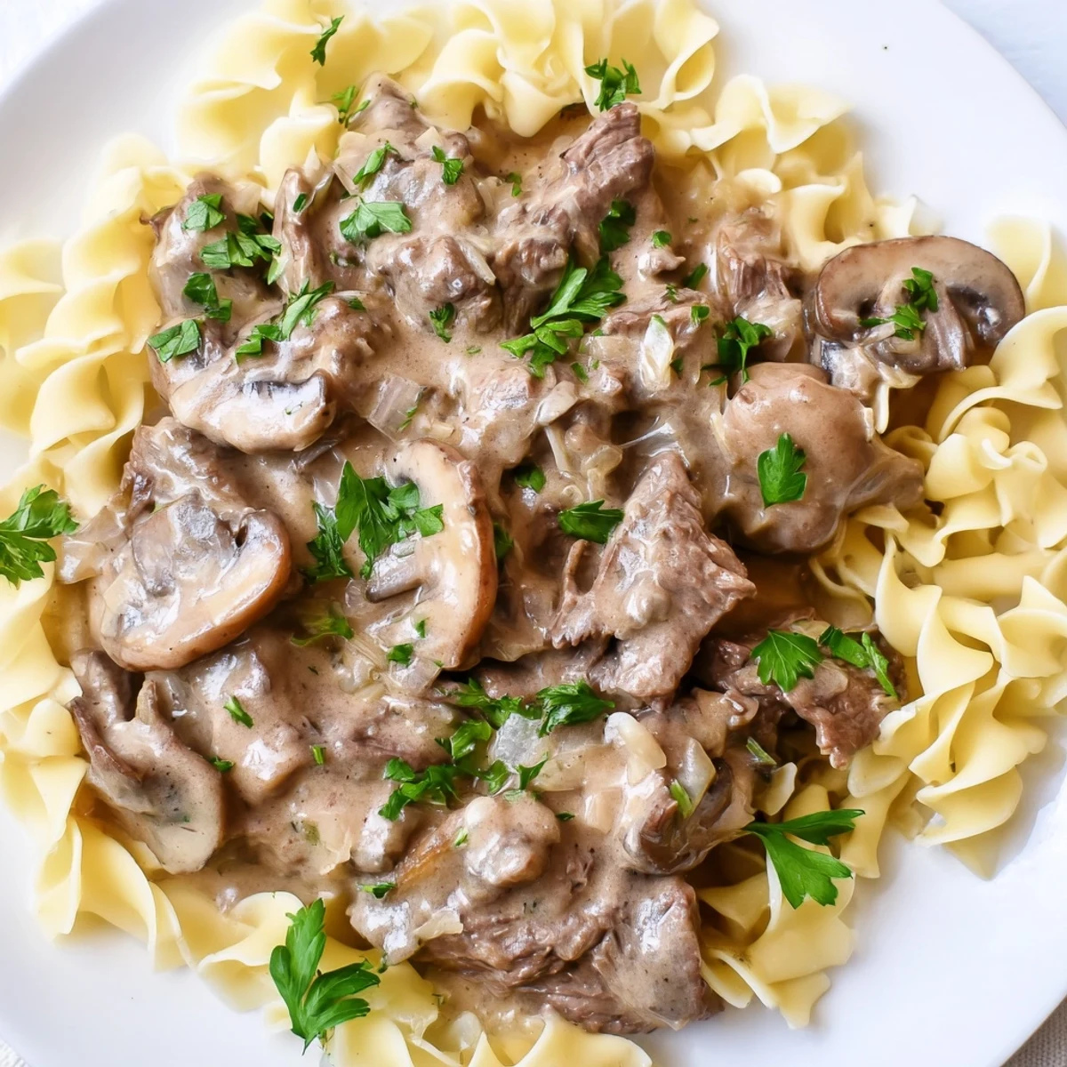 Steaming beef stroganoff over buttery egg noodles, featuring golden mushrooms and a rich, creamy sauce in a skillet.