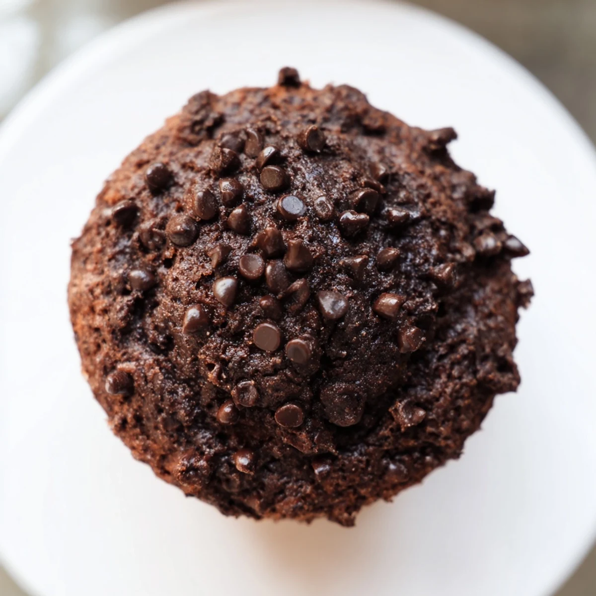 Two baked Chocolate Muffin Tops sit on a wire rack with melty chocolate chips and crackled, crisp edges.