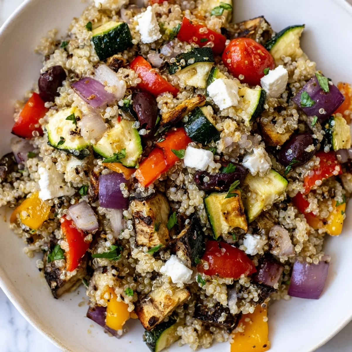 A wholesome Mediterranean Quinoa Salad topped with crumbled feta, kalamata olives, and fresh parsley sits on a rustic wooden table.