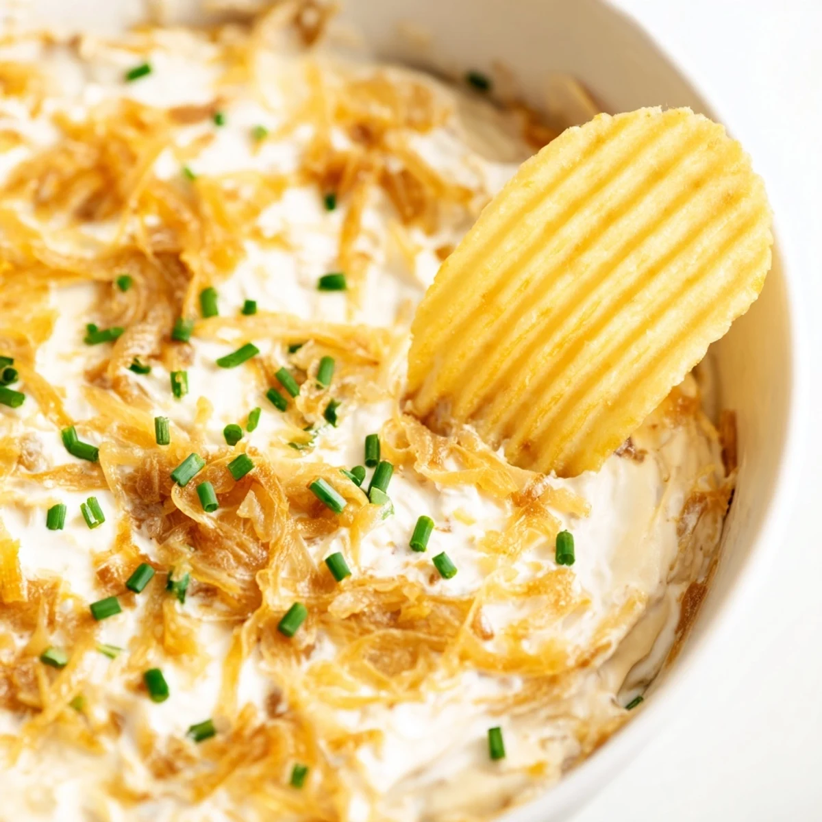 Hearty bowl of Game Day Onion Dip with golden onions and chives, paired with ridged potato chips for the ultimate party appetizer spread.