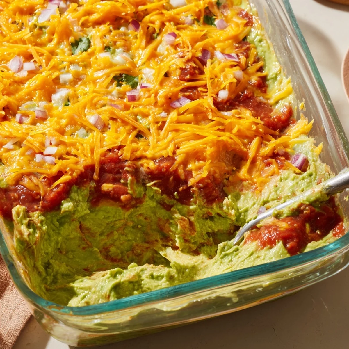 A vibrant Touchdown Tex Mex Layer Dip in a glass dish, featuring colorful layers of beans, guacamole, salsa, and melted cheese.