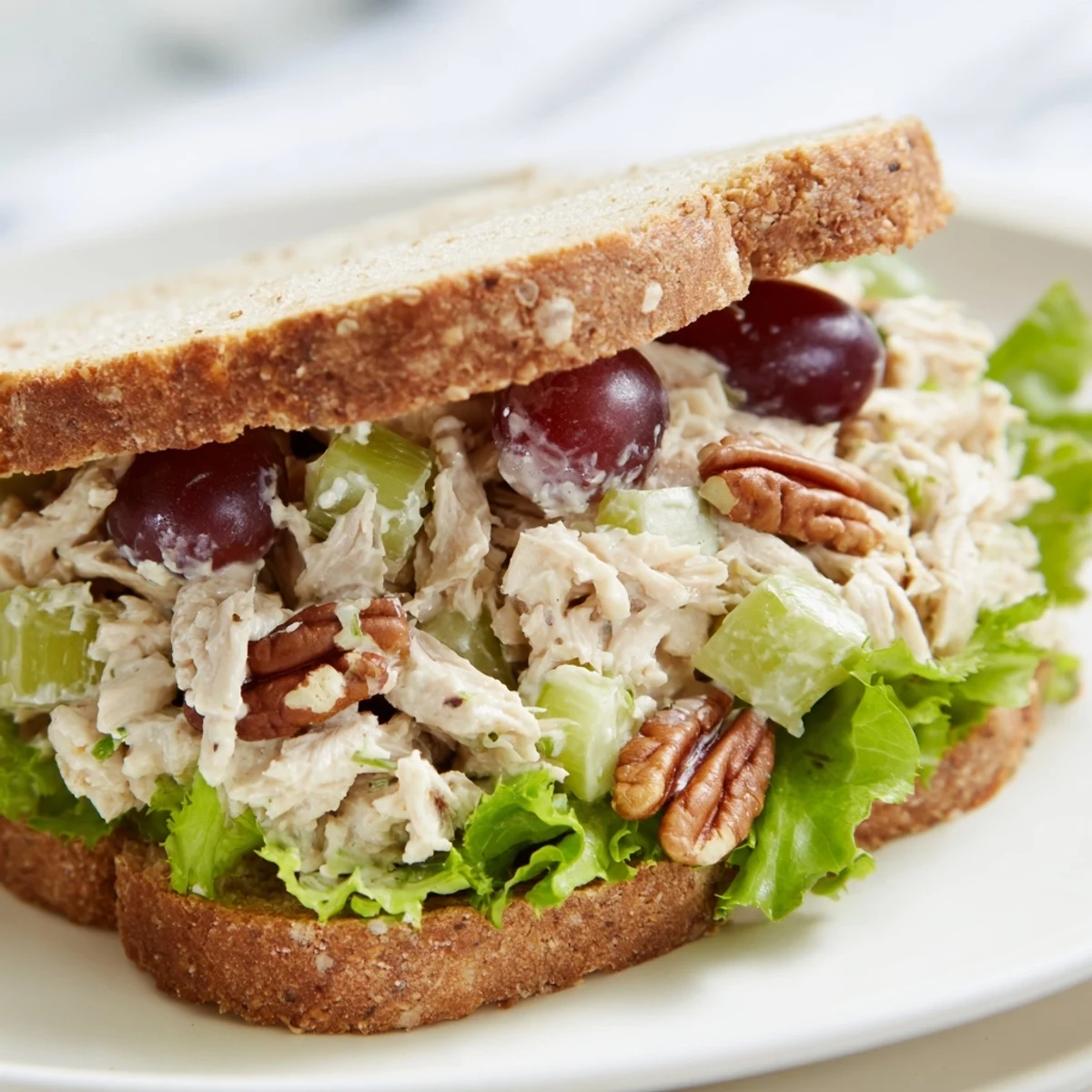 Vibrant chicken salad sandwich with halved red grapes, creamy dressing, and crisp lettuce on a toasted roll.  