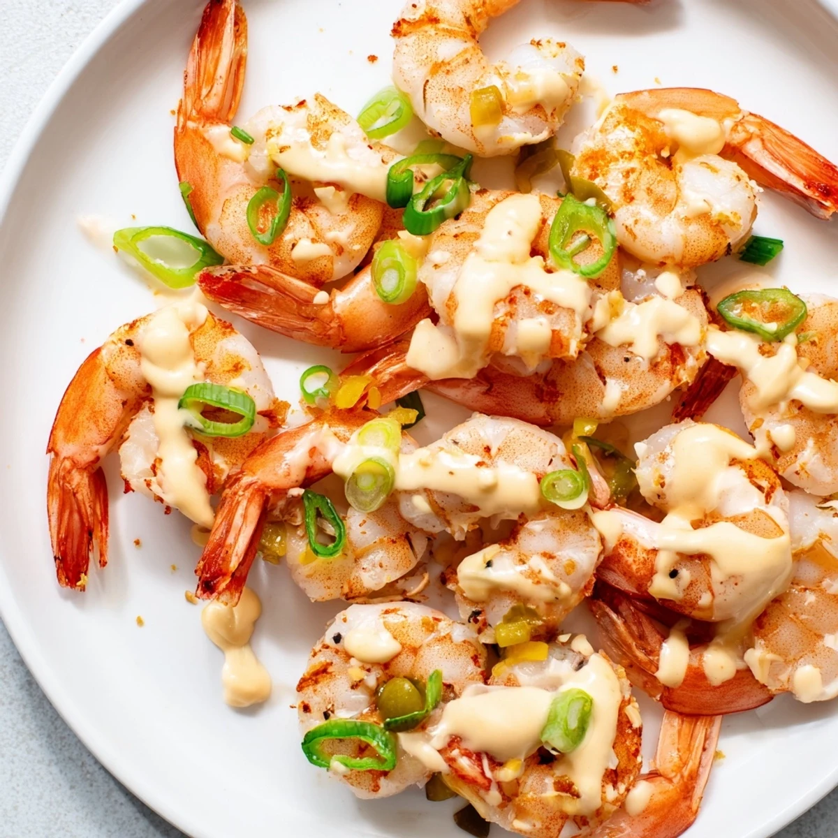 A close-up of tender shrimp coated in zesty Cajun Remoulade Sauce, garnished with celery and capers for texture.