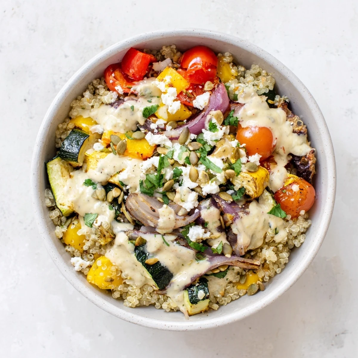 Vibrant bowl of Roasted Vegetable Quinoa Bowl garnished with feta, parsley, and pumpkin seeds, served on a rustic wooden table.  