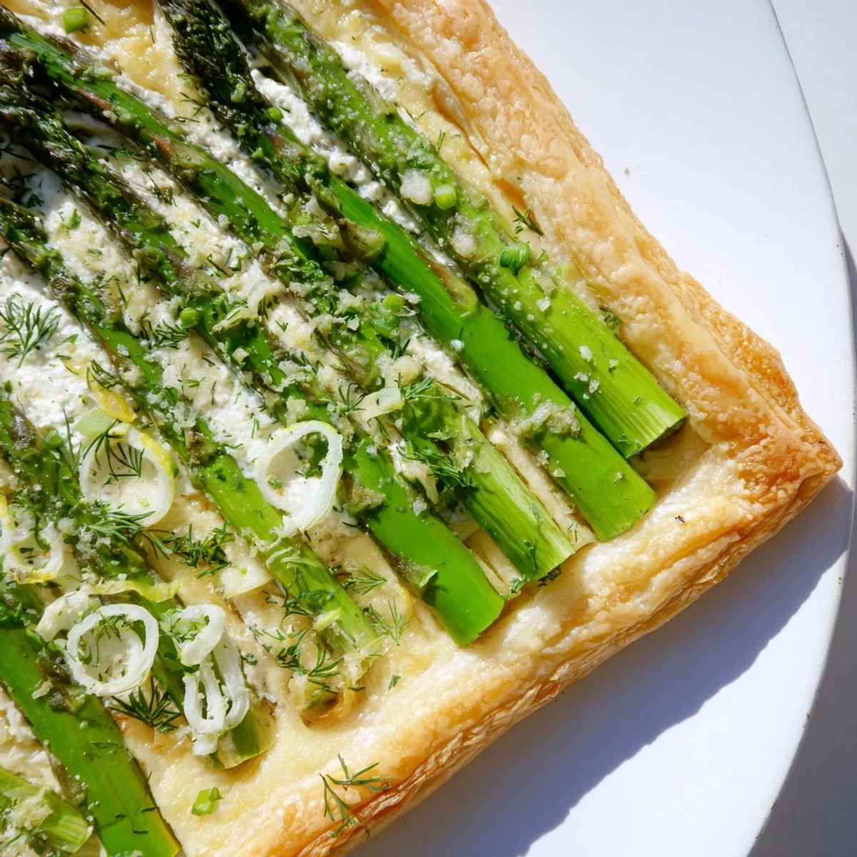 Golden-brown puff pastry topped with tender green asparagus spears, creamy cheese spread, and sliced spring onions on a baking sheet.  