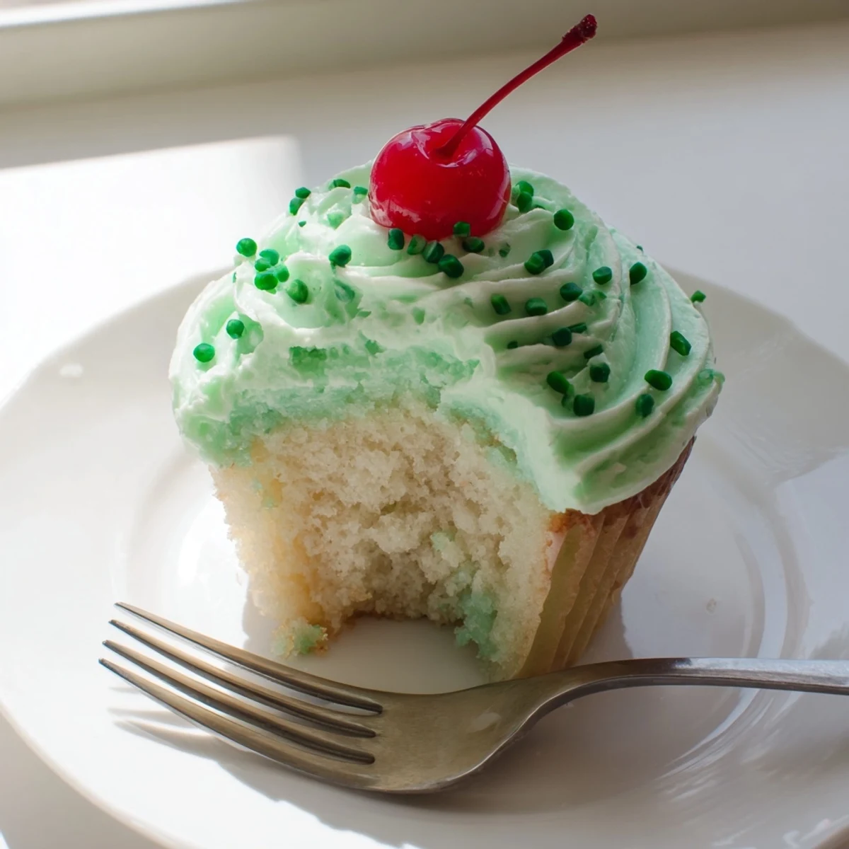 Stack of golden Shamrock Shake Cupcakes with creamy mint frosting, adorned with shimmering green sprinkles for St. Patrick's Day.