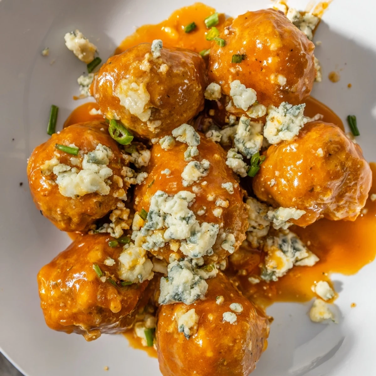 Golden baked chicken meatballs glistening with tangy Buffalo sauce and creamy crumbled blue cheese, ready to serve with crisp celery and carrot sticks for a classic party platter.