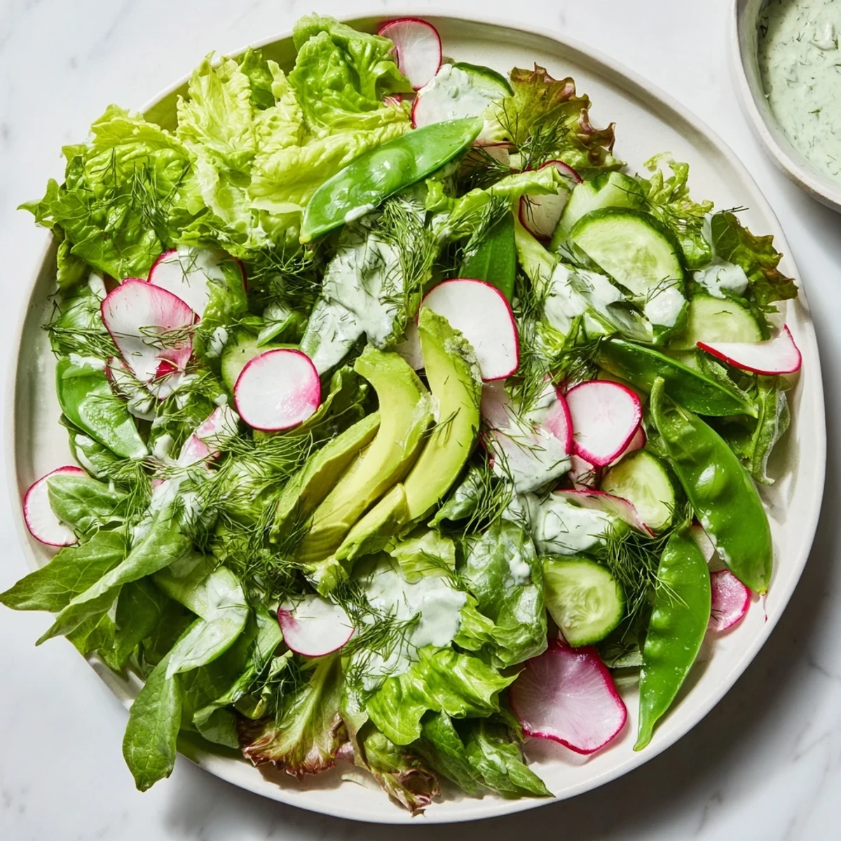 Freshly tossed Green Salad with Green Goddess Dressing, topped with sliced radishes and crisp snap peas on a plate.
