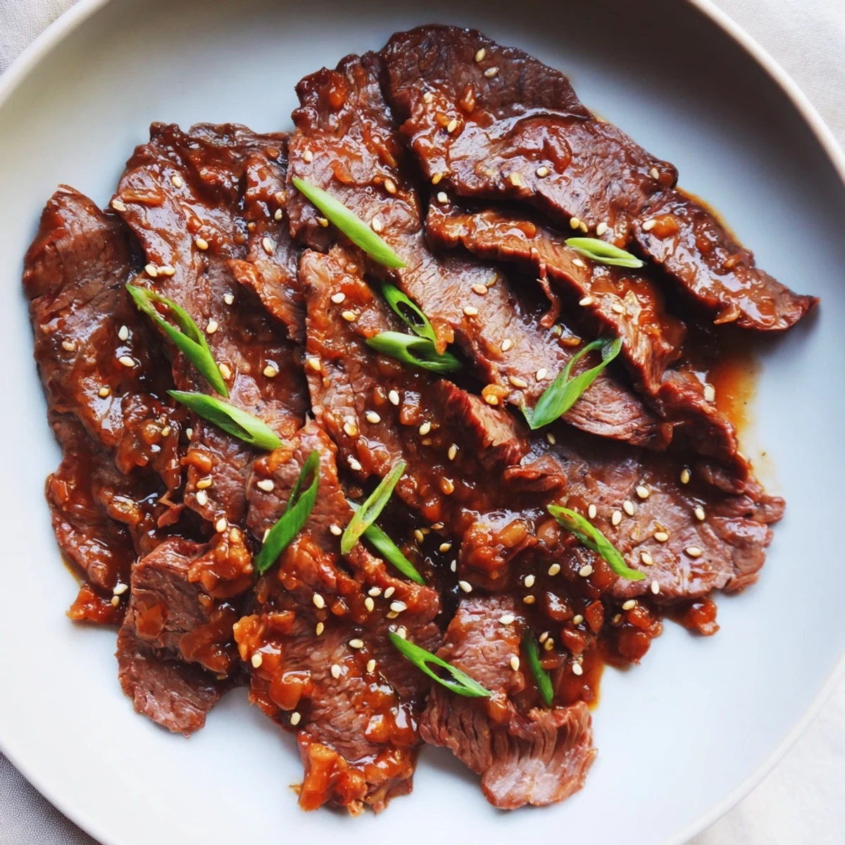 Tender slices of Ultimate Slow Cooker Mongolian Beef simmer in a rich savory sauce, garnished with green onions and sesame seeds.