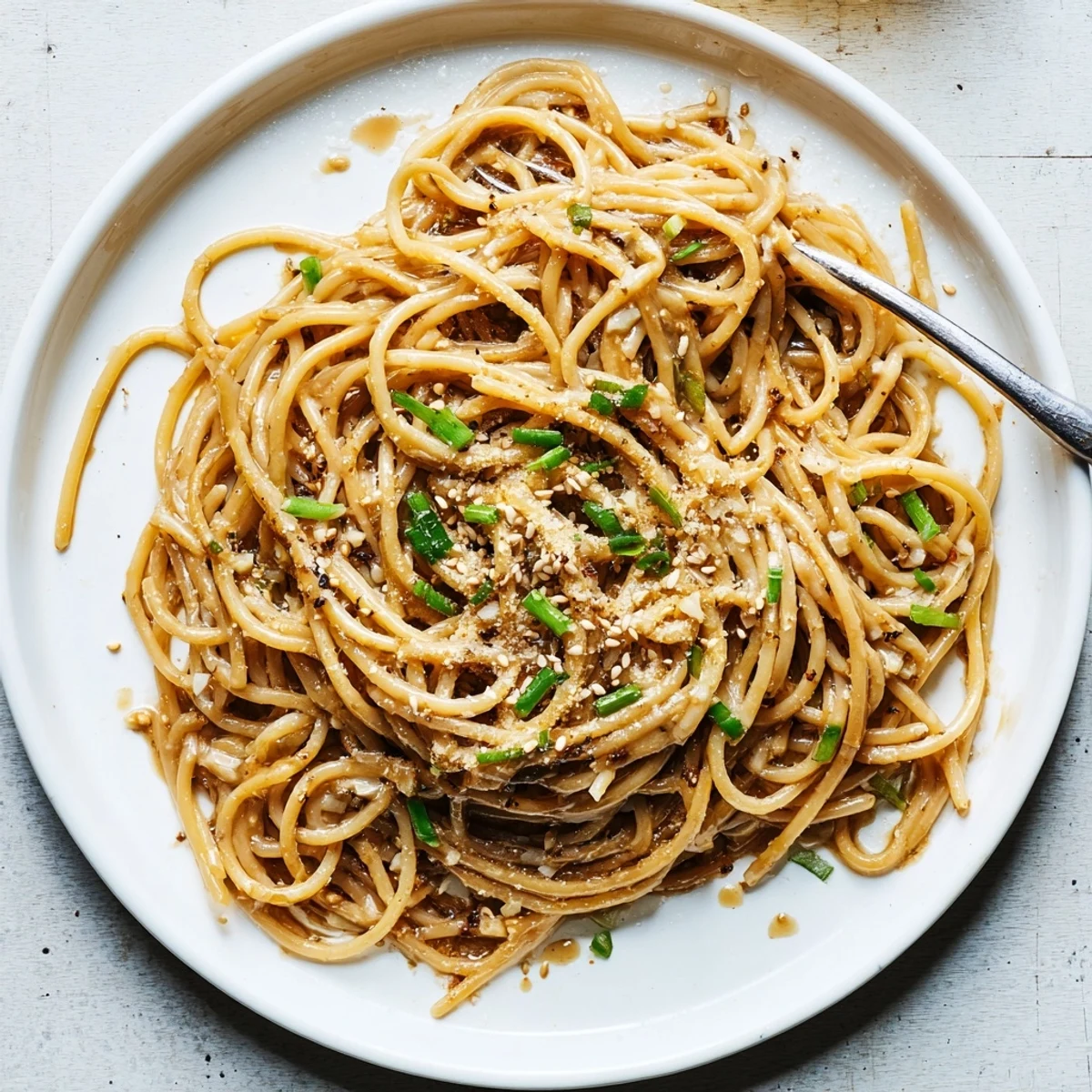 Steaming Garlic Noodles in a skillet with melted butter, minced garlic, and soy sauce garnished with scallions.