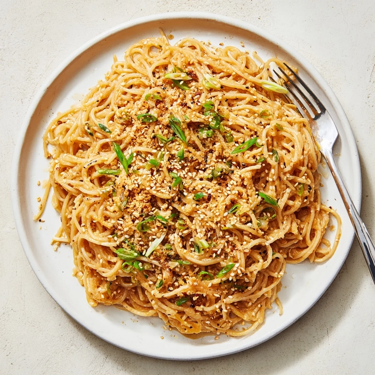 Golden Garlic Noodles tossed in a garlicky sauce with sesame seeds and Parmesan on a white plate.