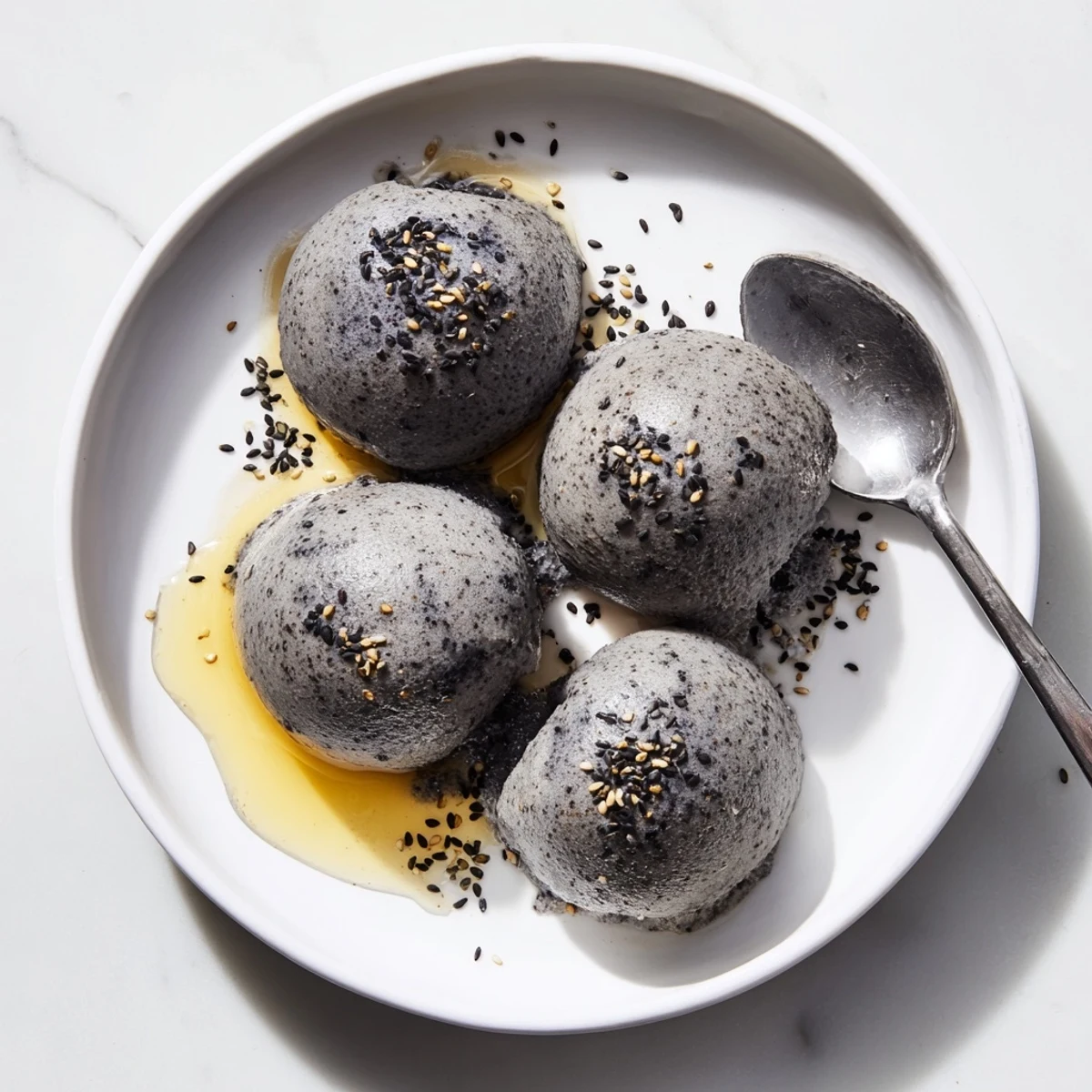 A scoop of Toasted Black Sesame Ice Cream in a ceramic bowl, topped with sesame seeds for extra crunch.
