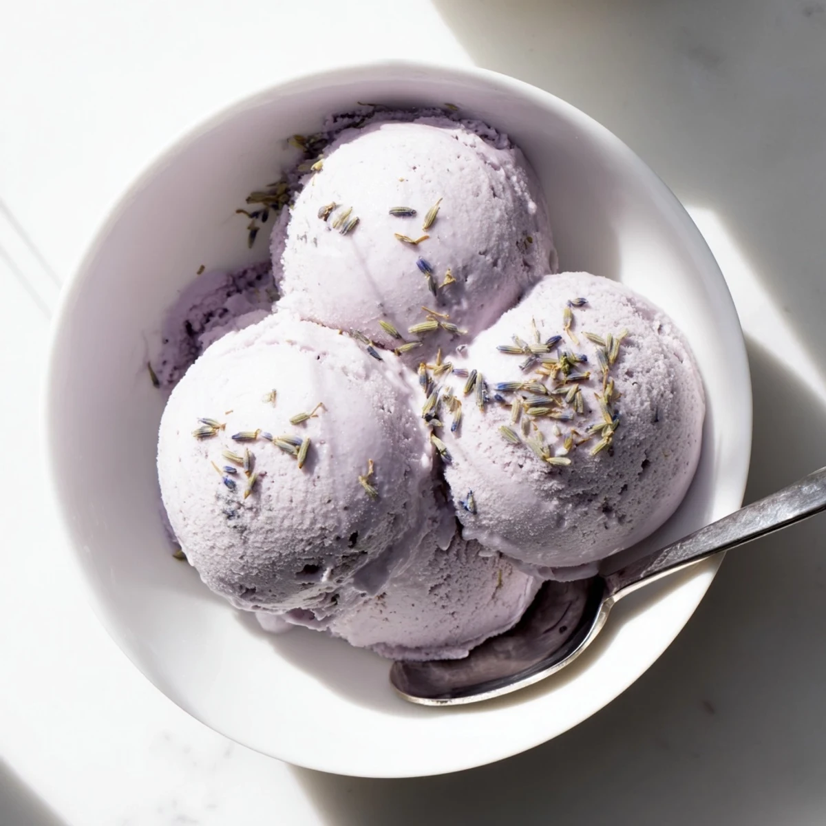 Creamy lavender ice cream with floral buds in a chilled bowl, ready for summer entertaining.