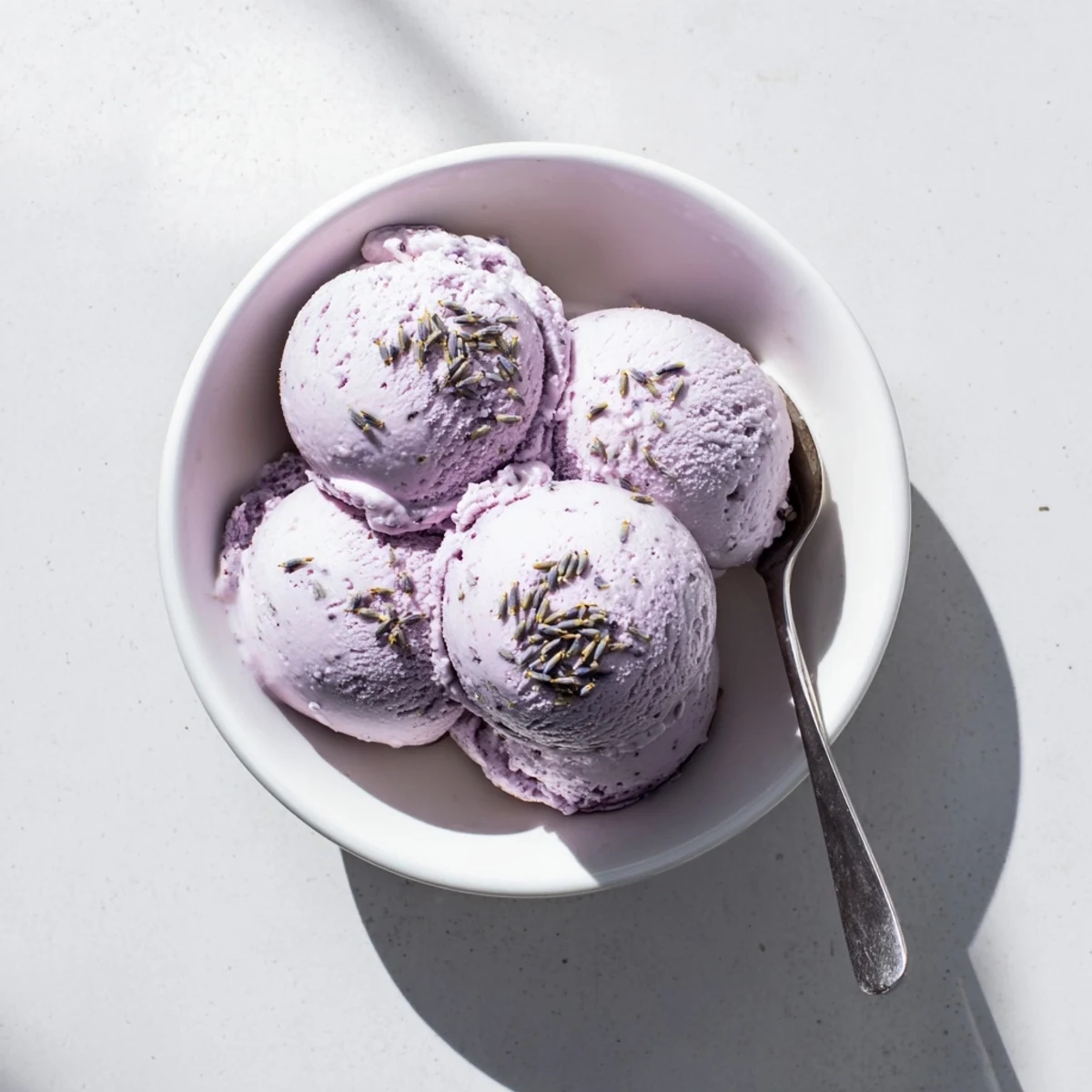 A scoop of lavender ice cream on a plate, garnished with edible flowers and cookies.