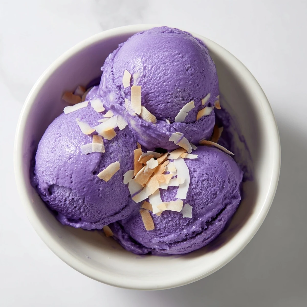 A close-up of vibrant purple Ube Ice Cream scoops in a glass dish, showing a smooth and creamy texture.