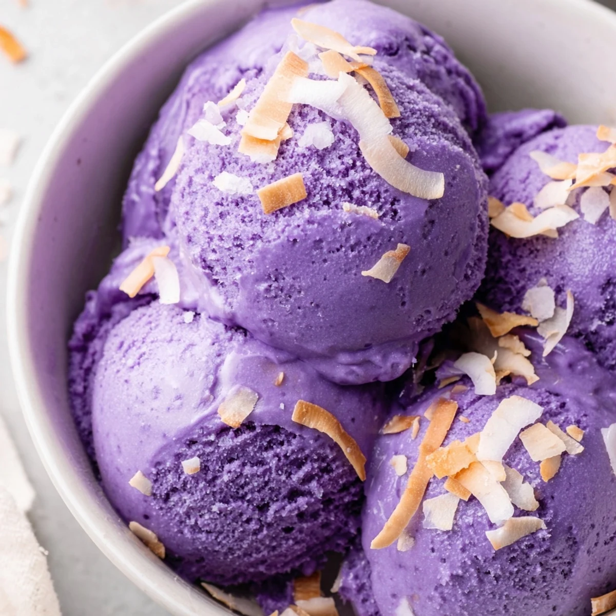 Creamy homemade Ube Ice Cream in a white bowl, topped with toasted coconut flakes for a sweet Filipino dessert.