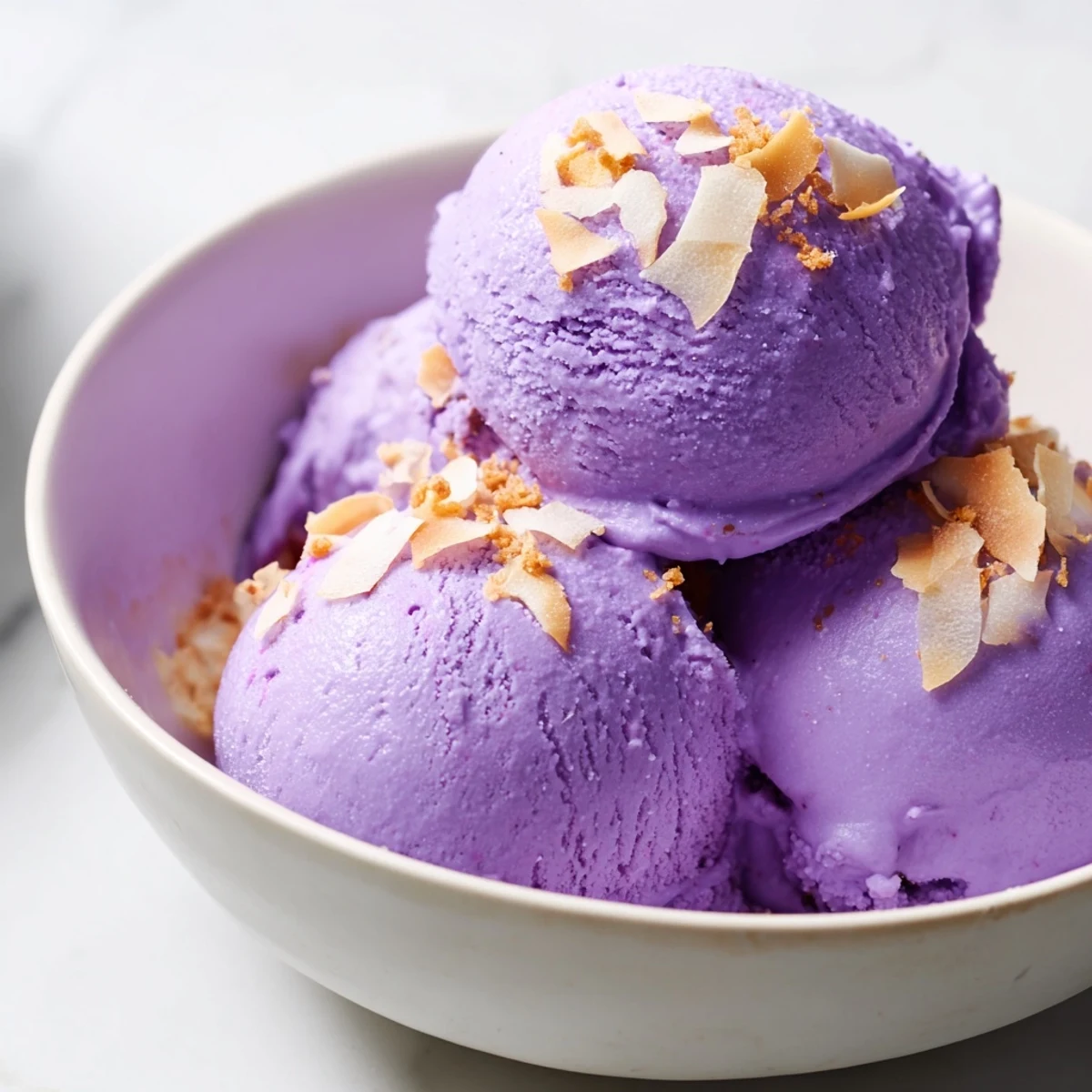 A single scoop of Ube Ice Cream placed on a wafer cookie, with fresh mint leaves adding a bright garnish.
