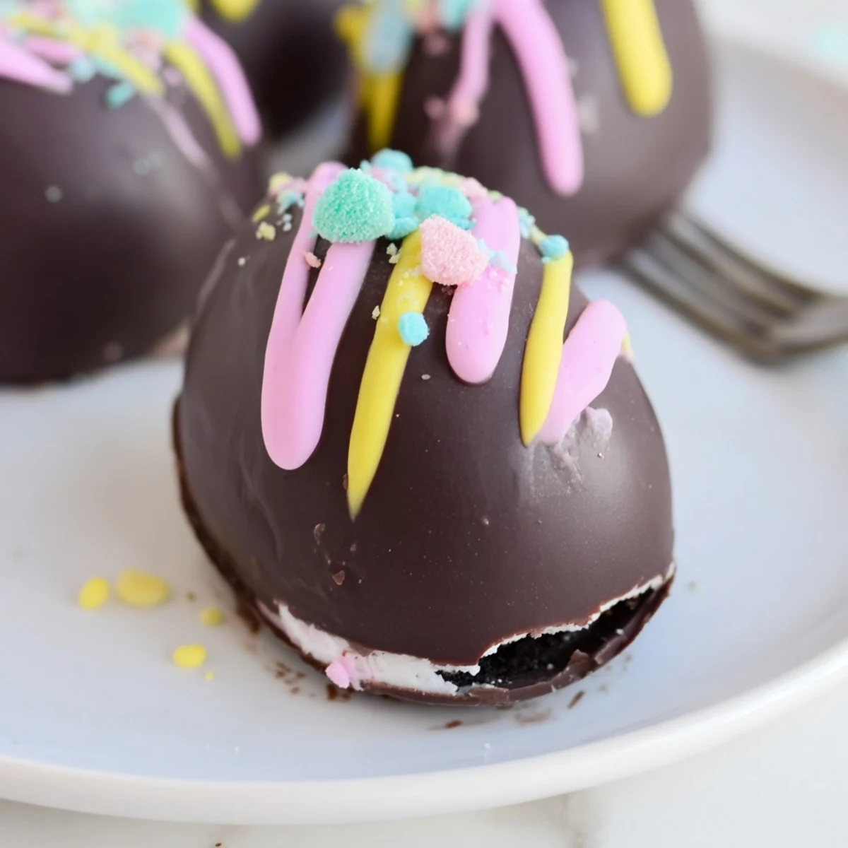 A hand dipping an Easter Egg Oreo Ball into melted chocolate, showing the creamy filling inside.