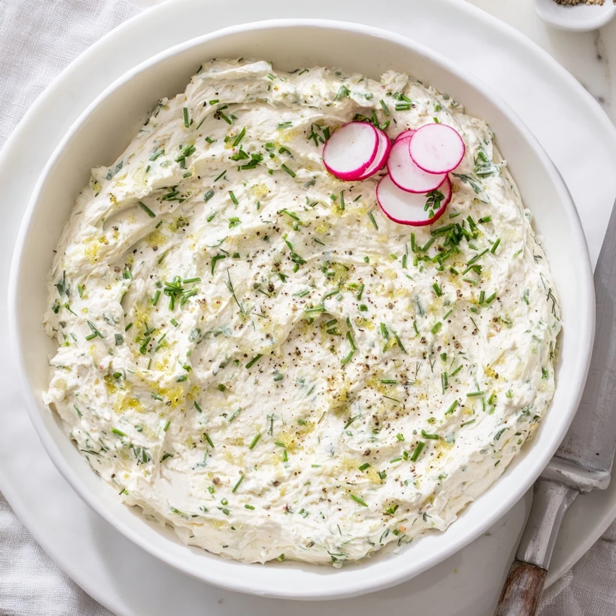 A close-up of the Simple Easter Herb Cheese Dip garnished with fresh chives, dill, and radish slices on a spring table.