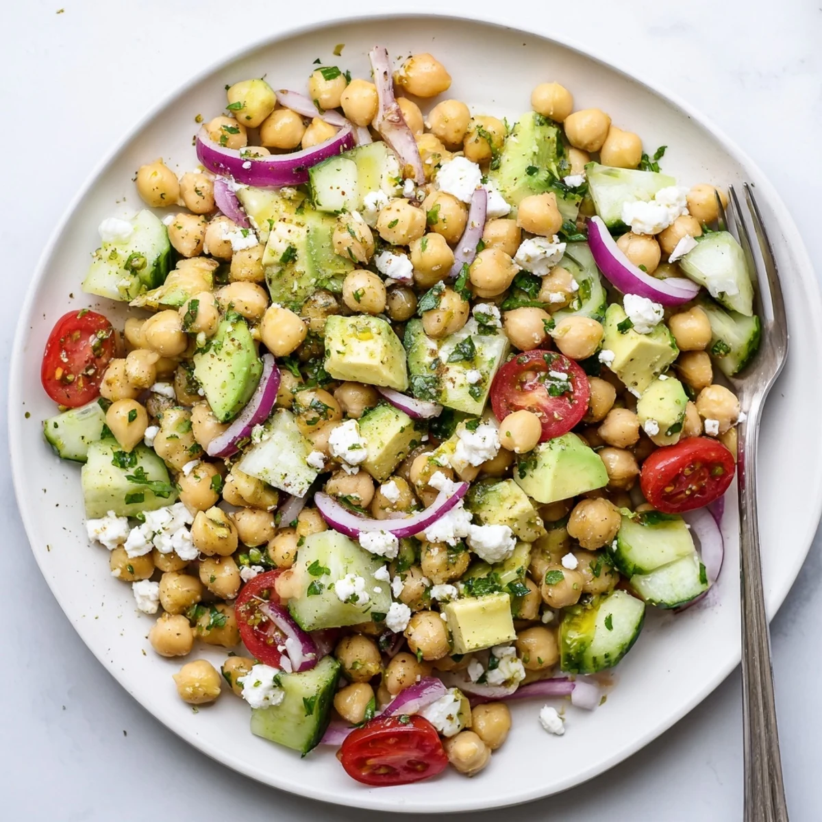 Close up view of Chickpea Feta Avocado Salad in a white bowl, showing diced cucumber and cherry tomatoes beside ripe avocado.