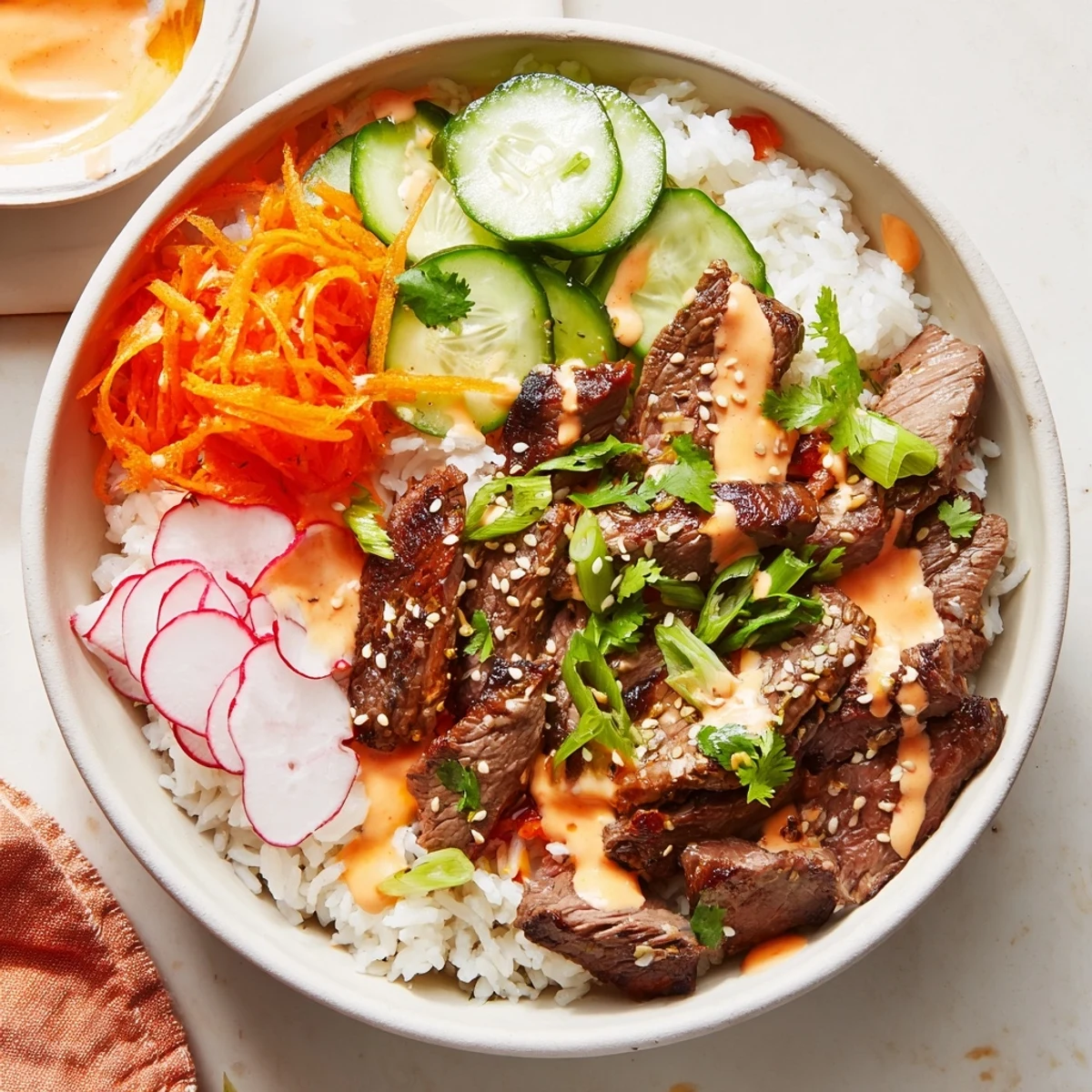 Steaming fluffy rice topped with caramelized steak and fresh veggies in Korean BBQ Steak Rice Bowls with Spicy Cream Sauce.