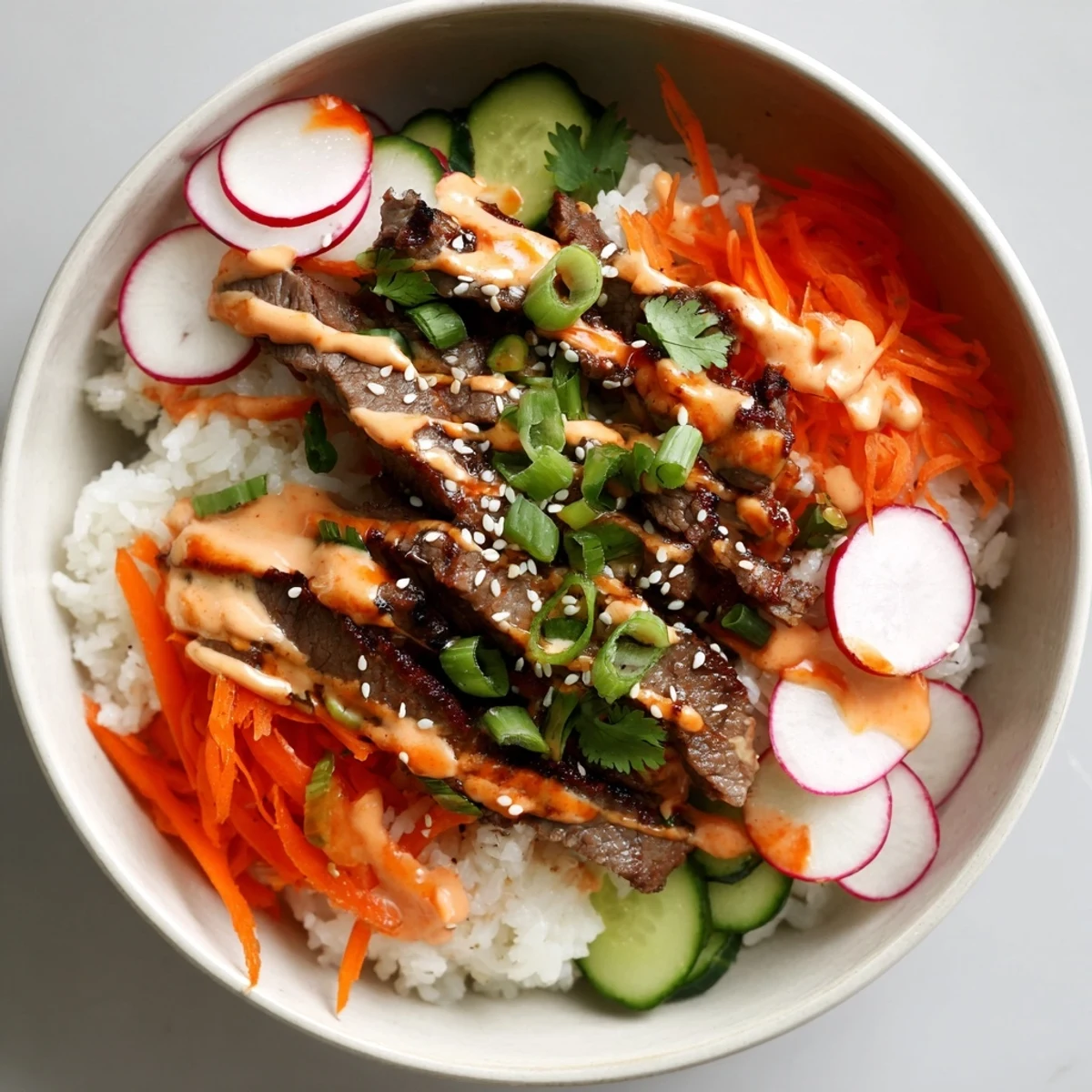 Golden slices of marinated steak over white rice with a creamy spicy drizzle in Korean BBQ Steak Rice Bowls.