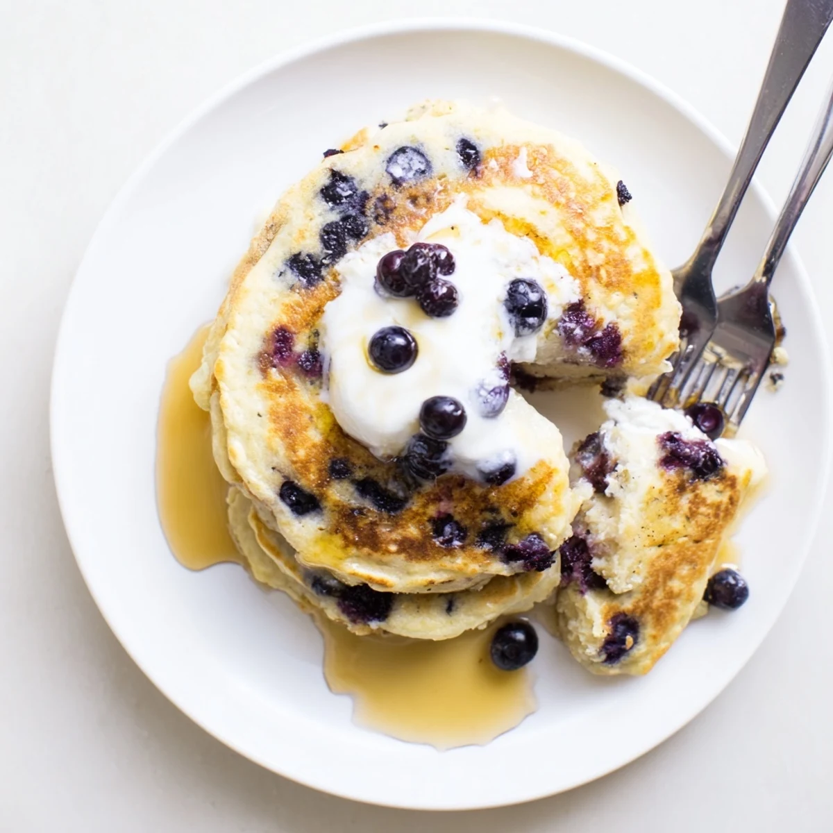 A close-up of Greek Yogurt Blueberry Pancakes served with a dollop of yogurt and a drizzle of honey.