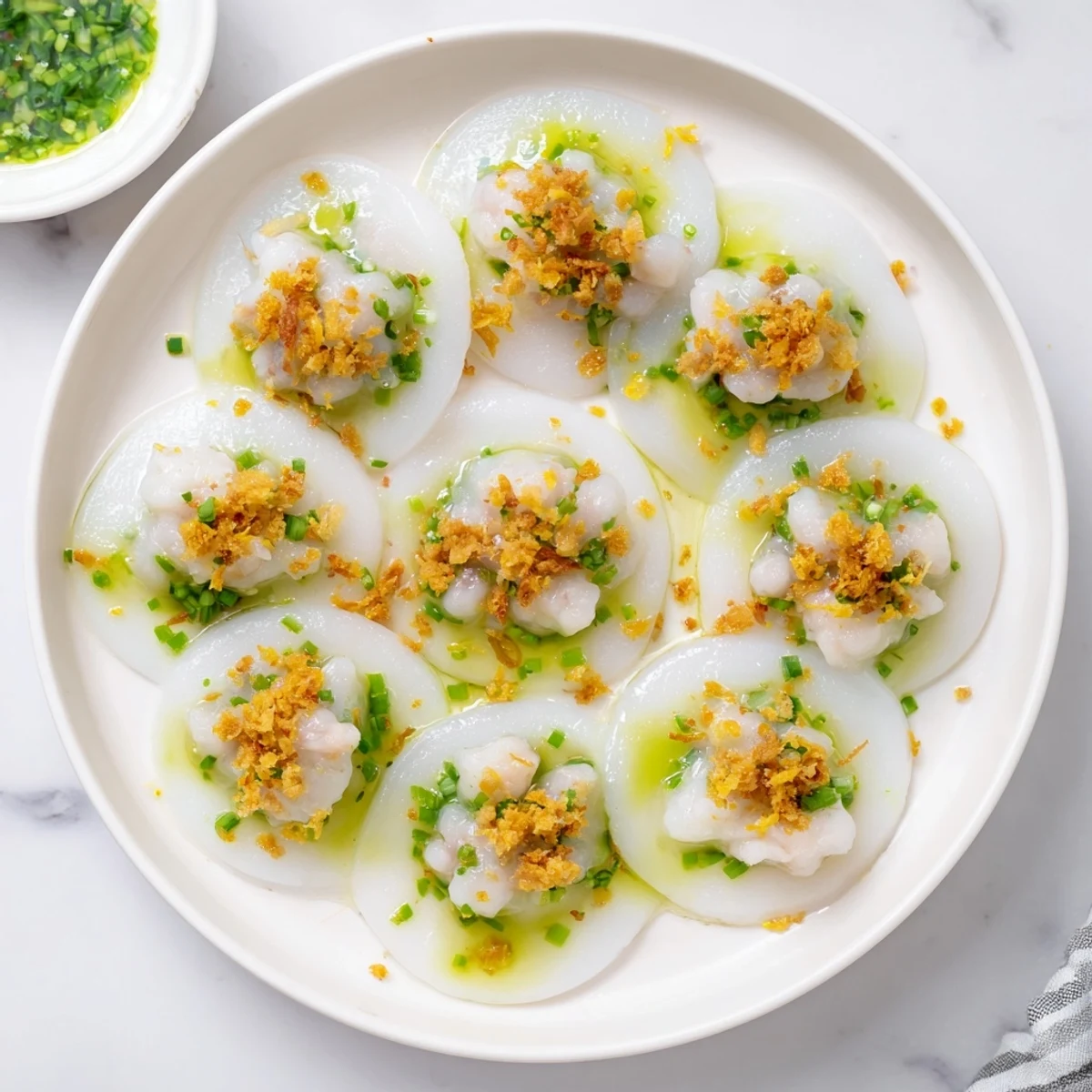 White steamed Banh Beo rice cakes topped with golden shrimp and fragrant scallion oil in small ceramic dishes