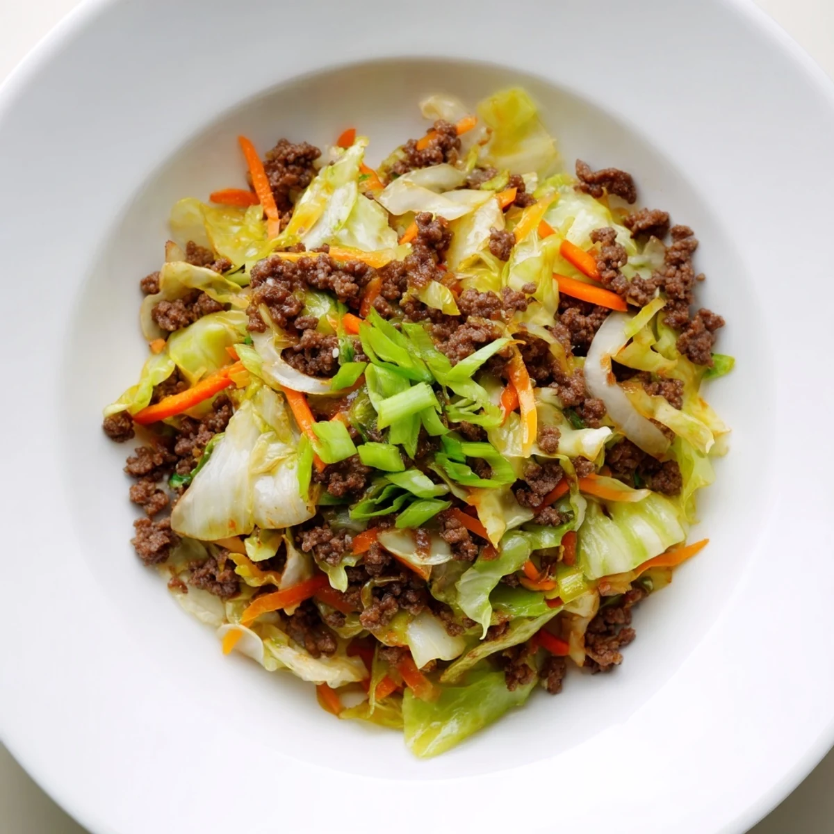 Golden brown ground beef and cabbage stir fry served in a white bowl with fresh green onion garnish