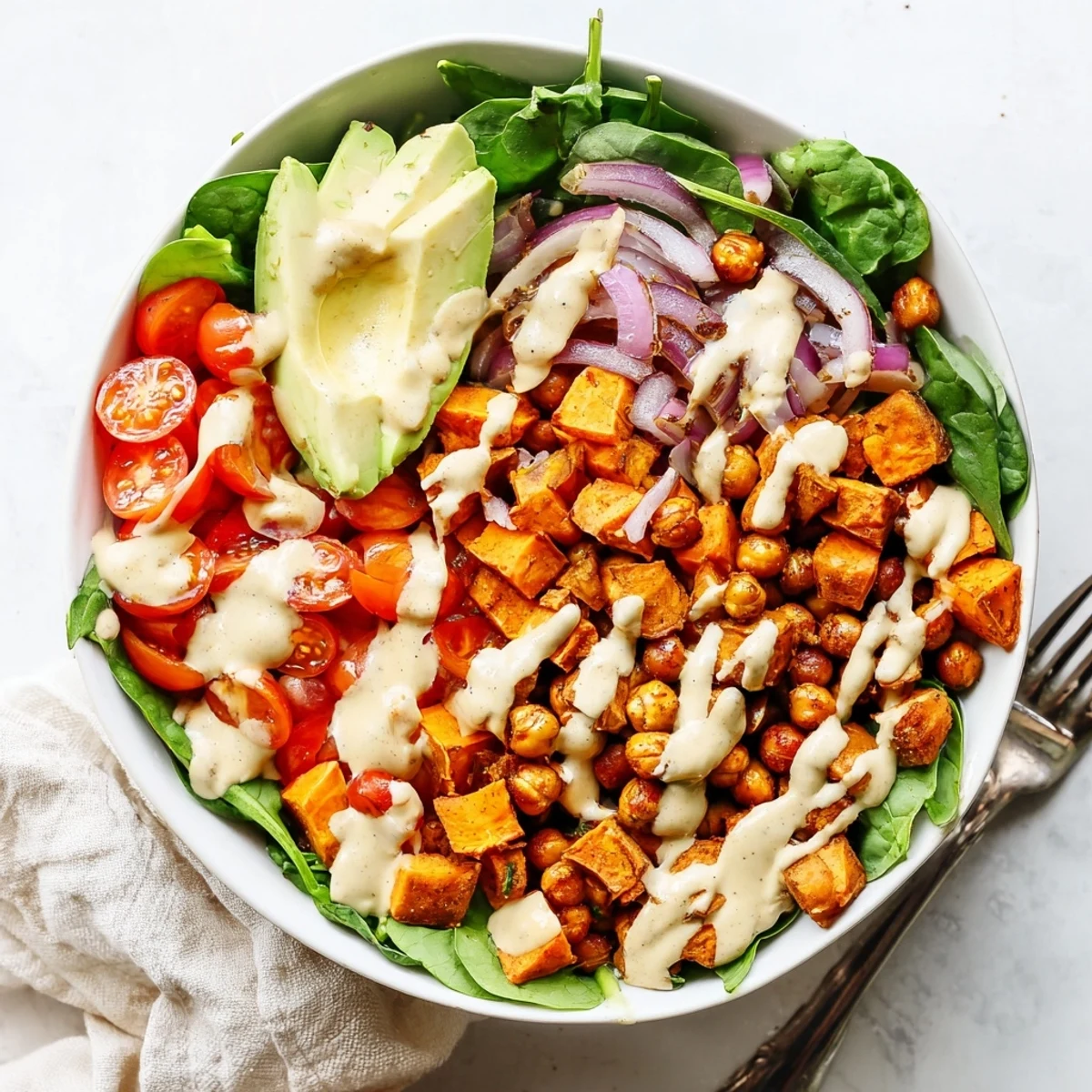 Colorful hearty sweet potato bowl featuring roasted chickpeas, spinach, tomatoes, and tangy tahini dressing