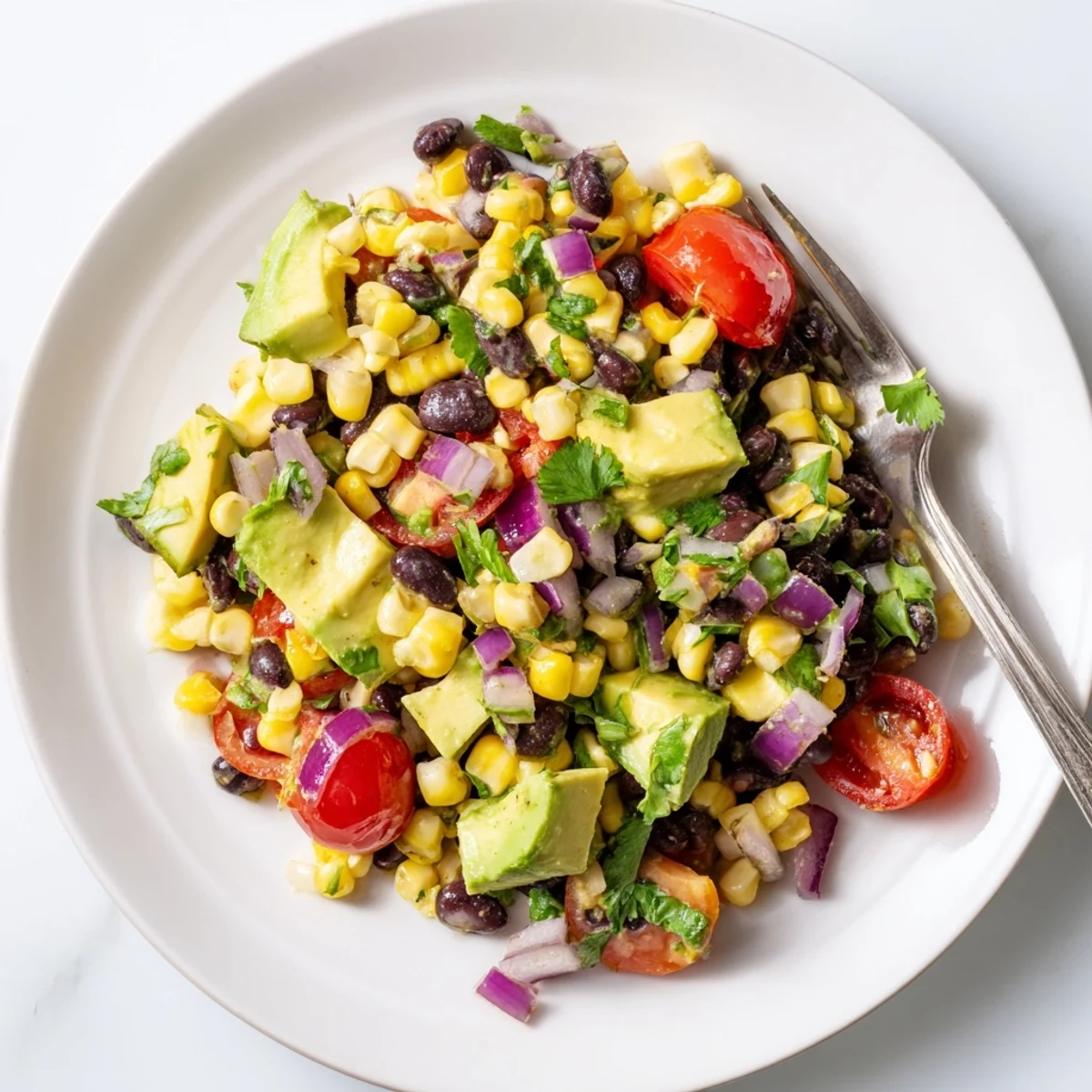 Colorful corn and black bean salad topped with creamy avocado cubes and served beside lime wedges on a rustic wooden cutting board.