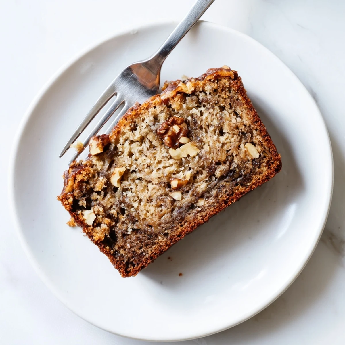 Moist best ever banana bread slice topped with melting butter on a white plate