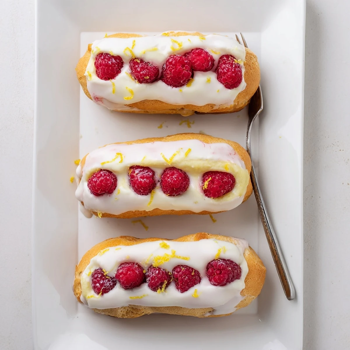 French pastry lemon raspberry éclairs with light lemon glaze and plump raspberry garnish for elegant dessert serving