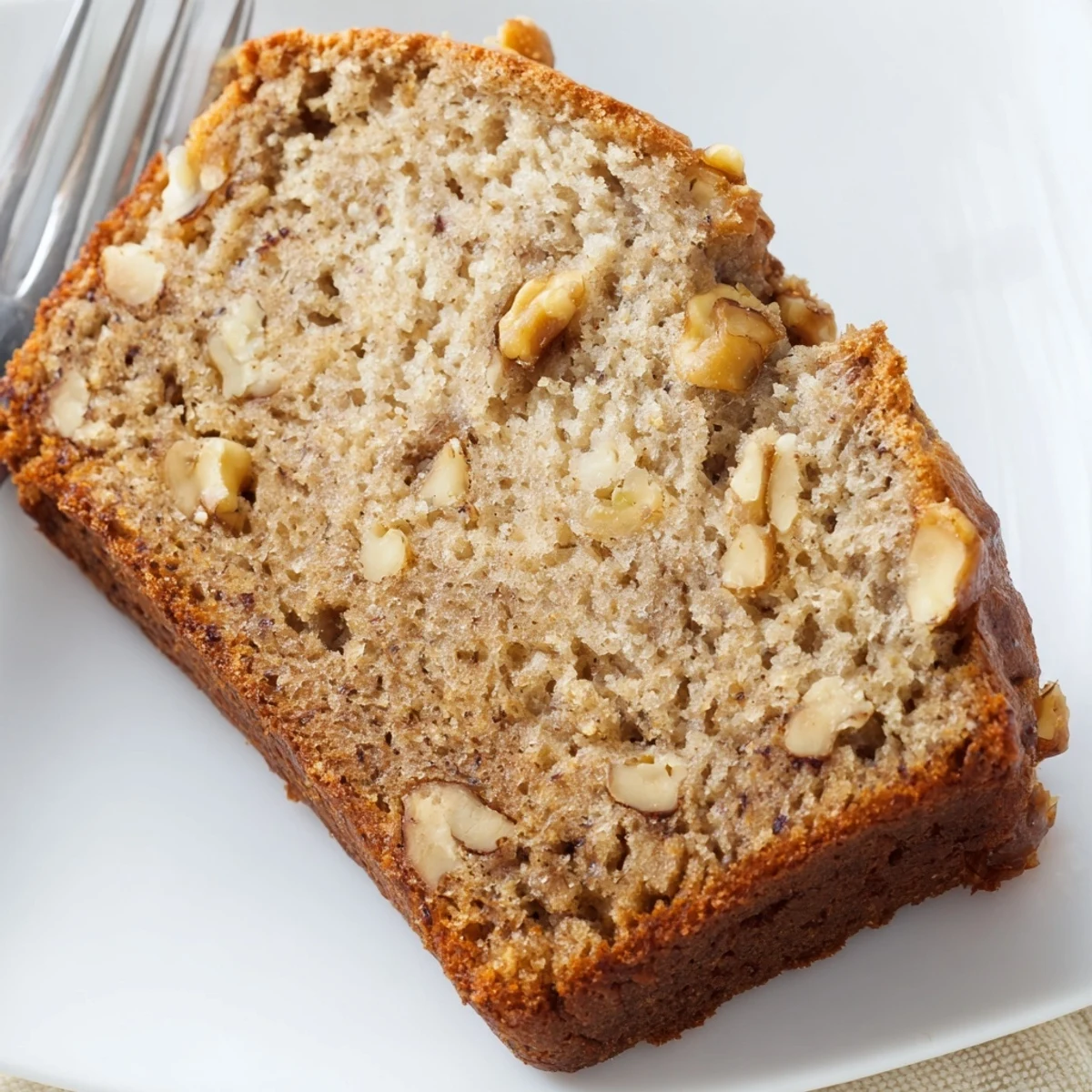Golden brown ultimate banana nut bread loaf studded with toasted walnuts on a rustic wooden board