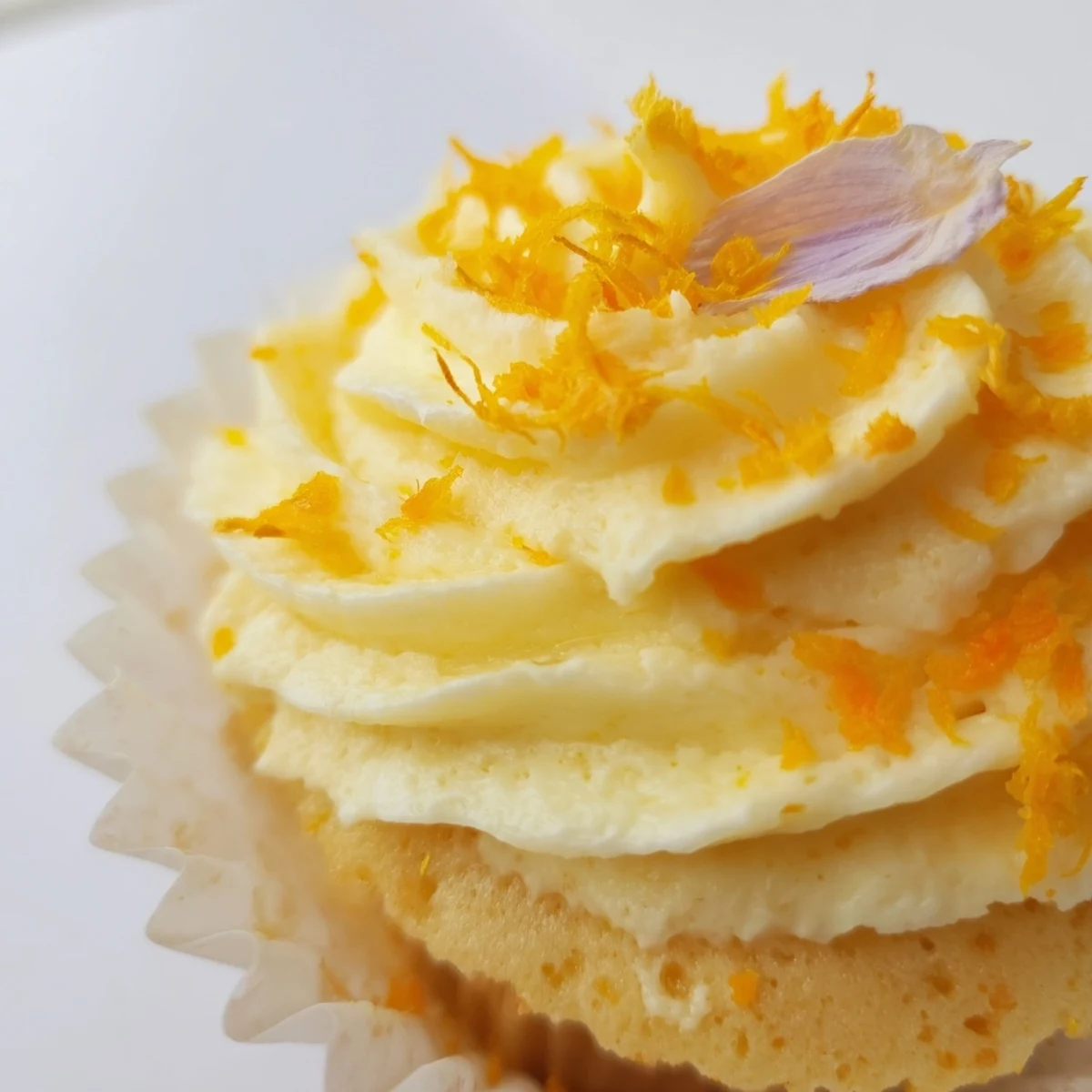 Moist orange blossom cupcakes on a white plate decorated with edible flowers and zesty frosting