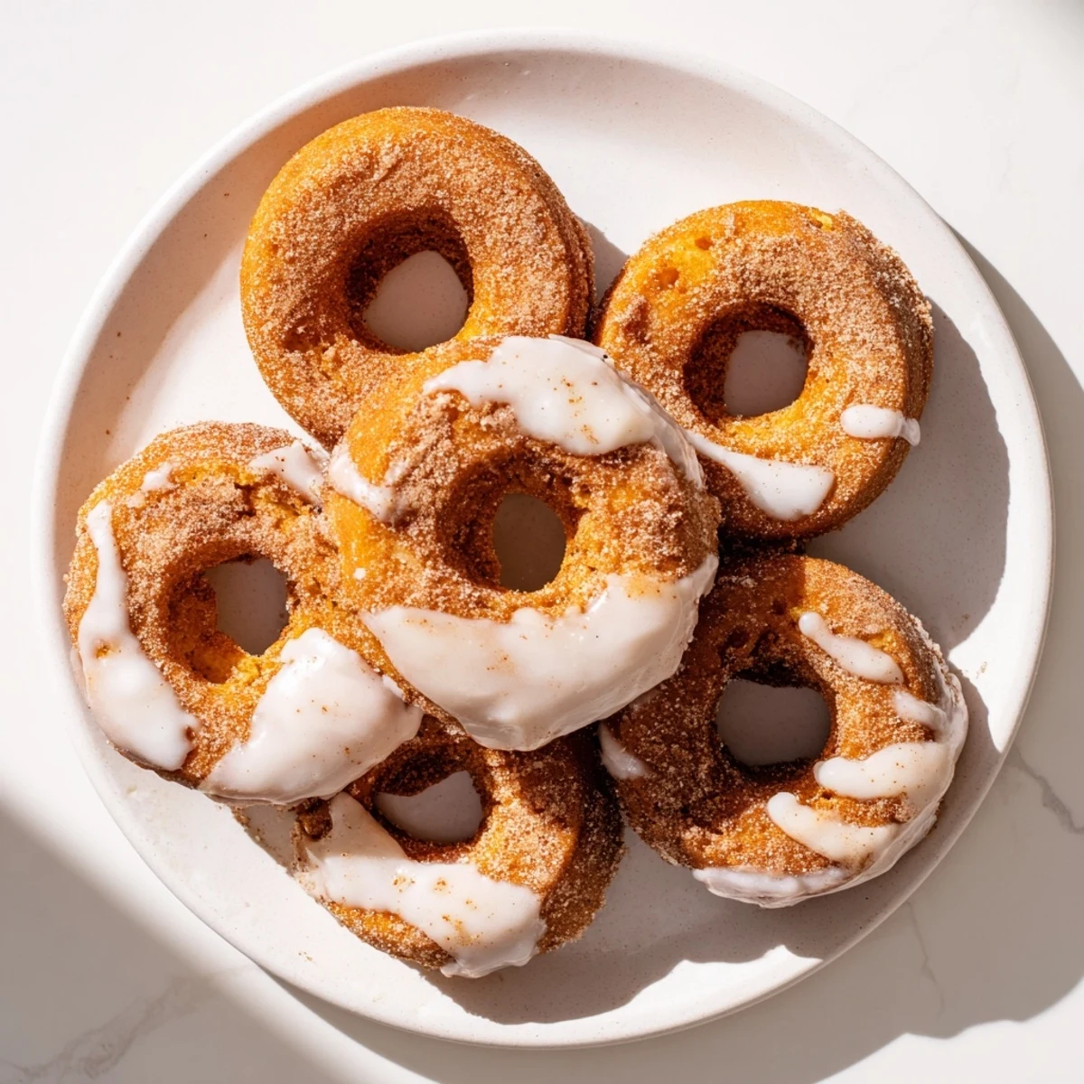 Golden pumpkin spice biscuit donuts coated in cinnamon sugar with sweet vanilla glaze drizzled over the fluffy fried pastries