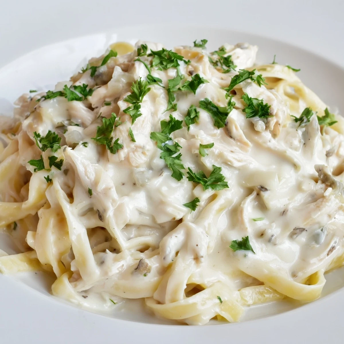Golden slow cooker Chicken Alfredo topped with fresh parsley and grated Parmesan cheese