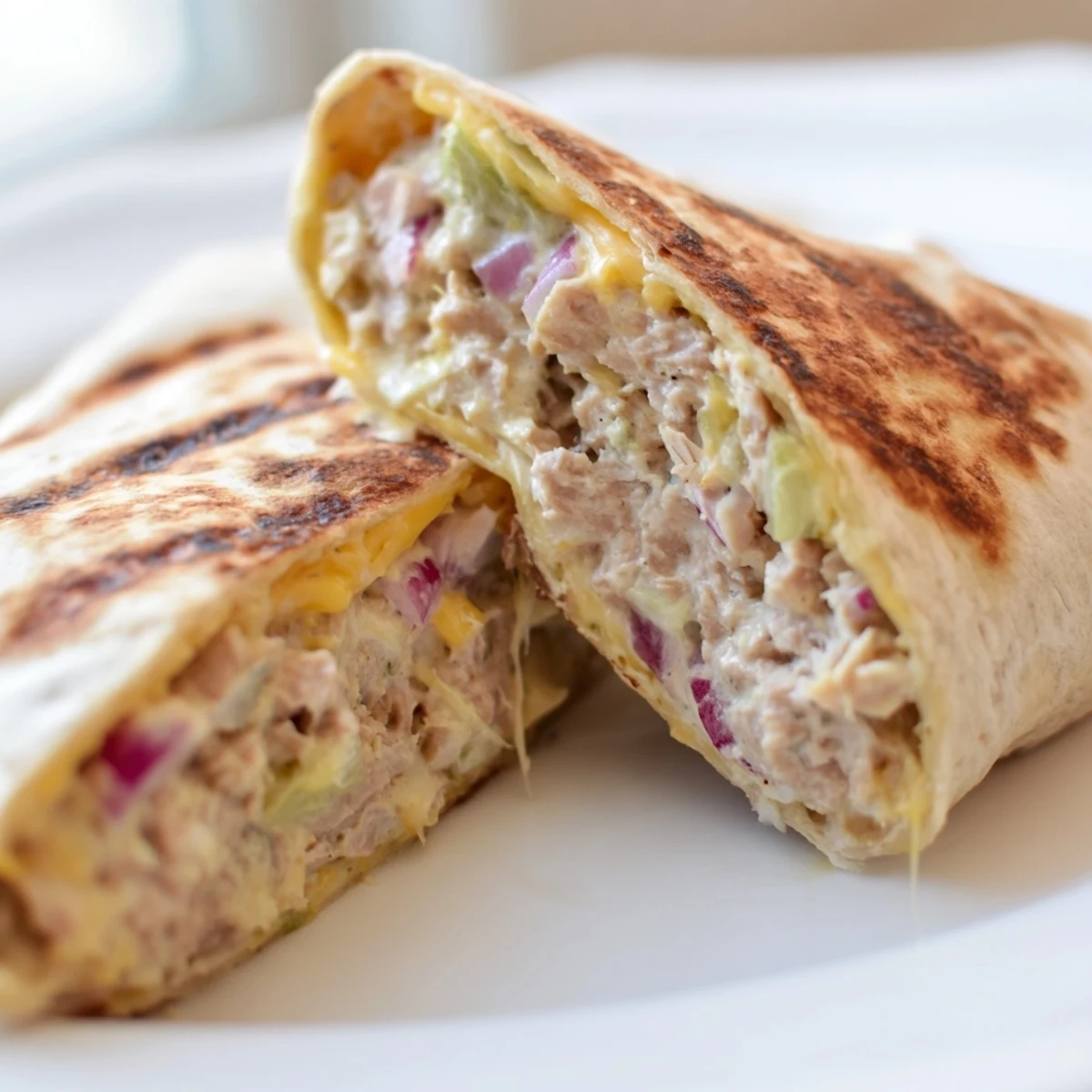 Golden brown tuna melt wrap with melted cheddar cheese oozing from warm grilled tortilla