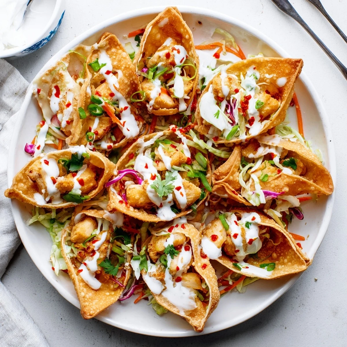 Golden crispy chicken wonton tacos topped with colorful slaw and zesty Asian sauce drizzle
