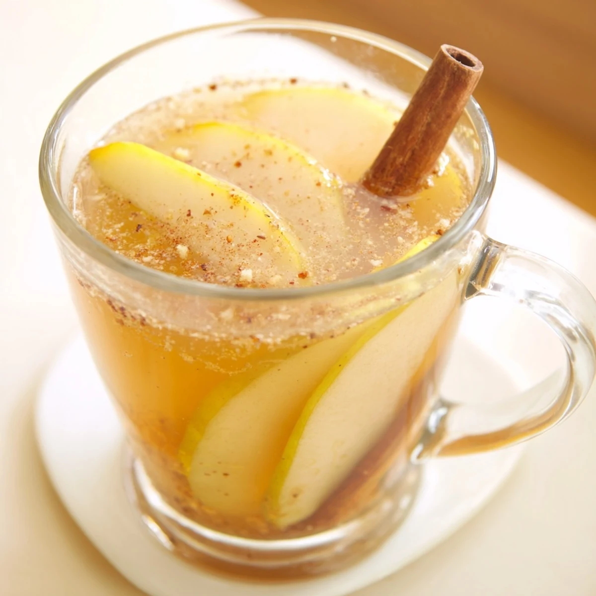 Golden brown spiced pear cider served in clear glass mugs with floating fruit pieces