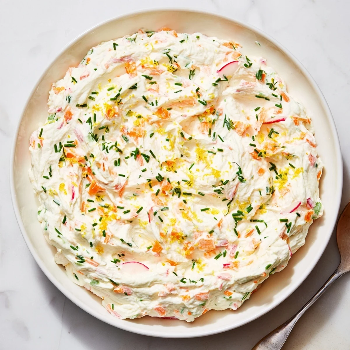 Festive white herb dip garnished with chopped chives and dill, accompanied by crisp carrot sticks and radishes