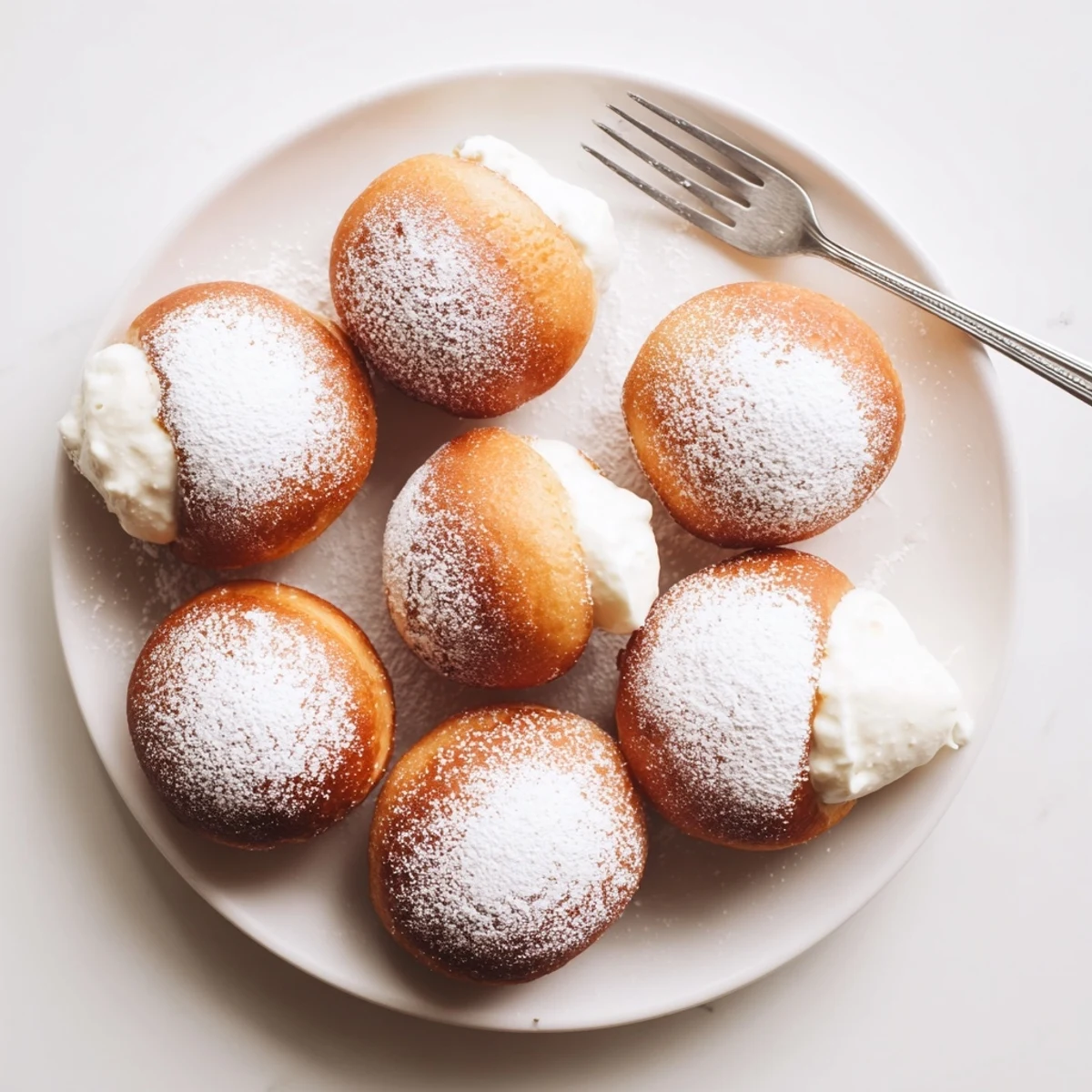 Golden brown Korean milk cream donuts dusted with powdered sugar on a white plate