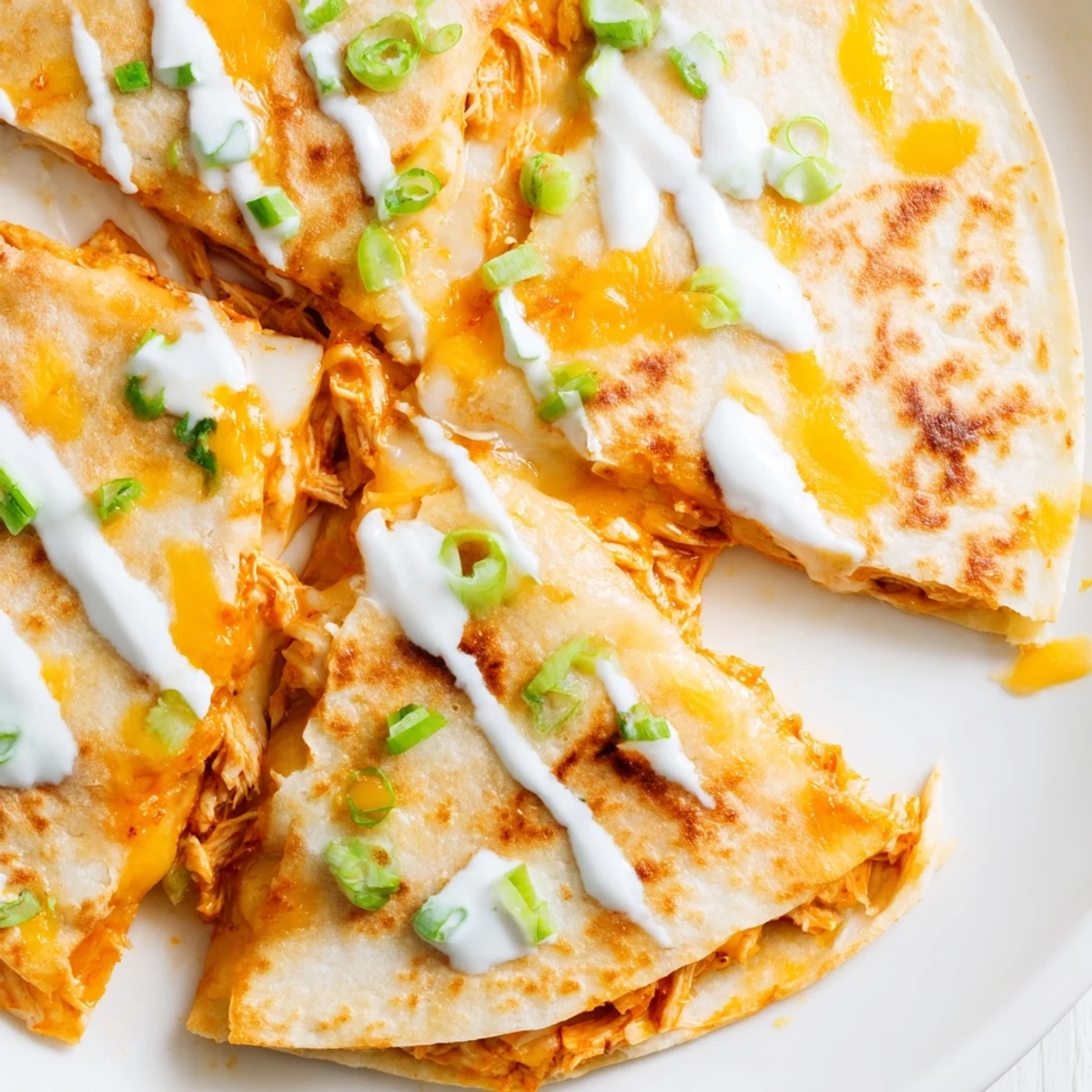 Golden buffalo chicken quesadillas sliced into wedges with white ranch drizzle on top