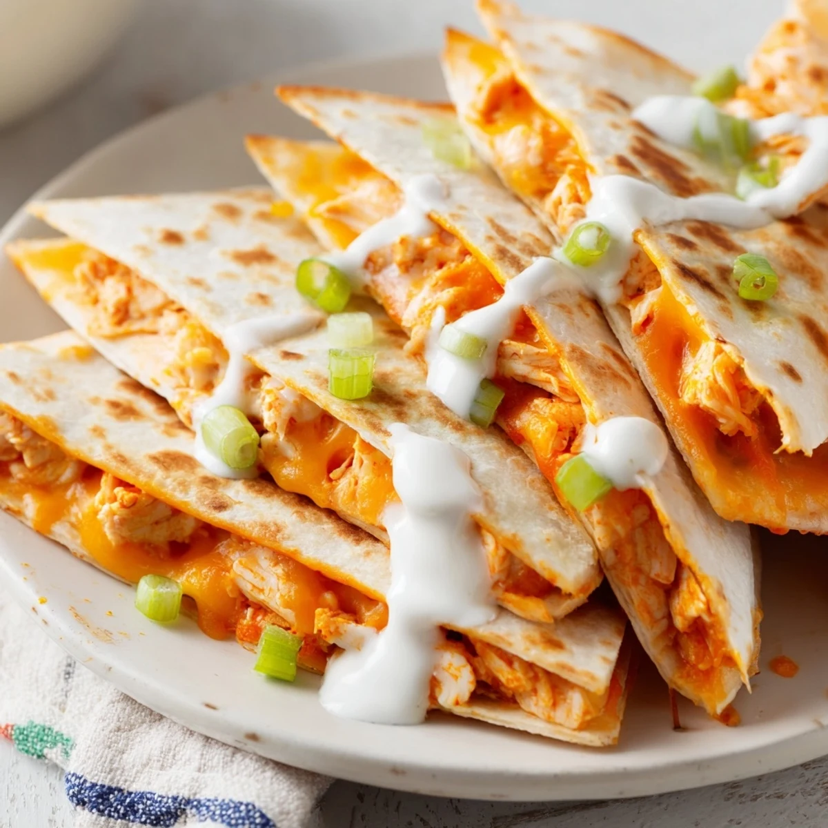 Plate of buffalo chicken quesadillas topped with cooling ranch drizzle and fresh green onion garnish