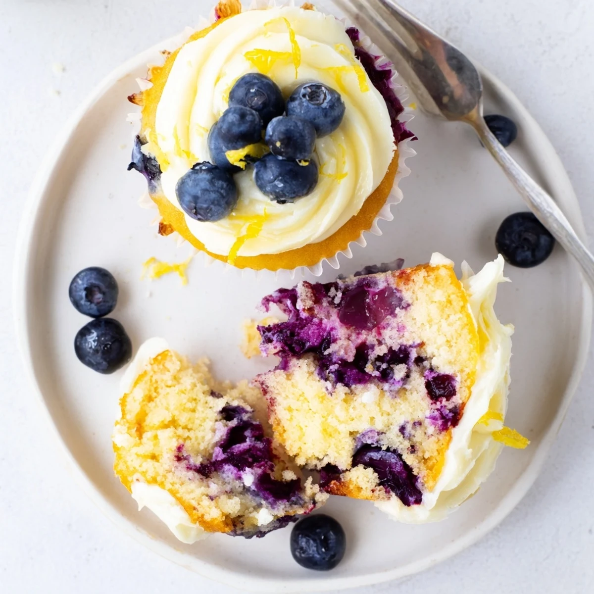 Fresh lemon blueberry cupcakes topped with creamy lemon frosting on a white plate