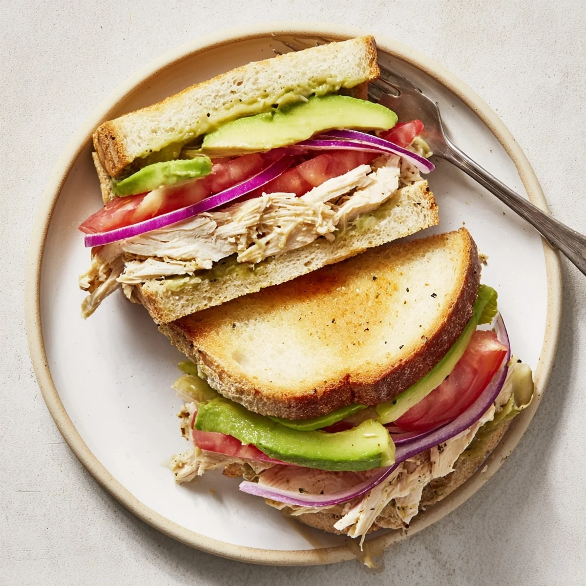 Sliced chicken avocado melt sandwich on a plate showing layers of tomato and creamy avocado