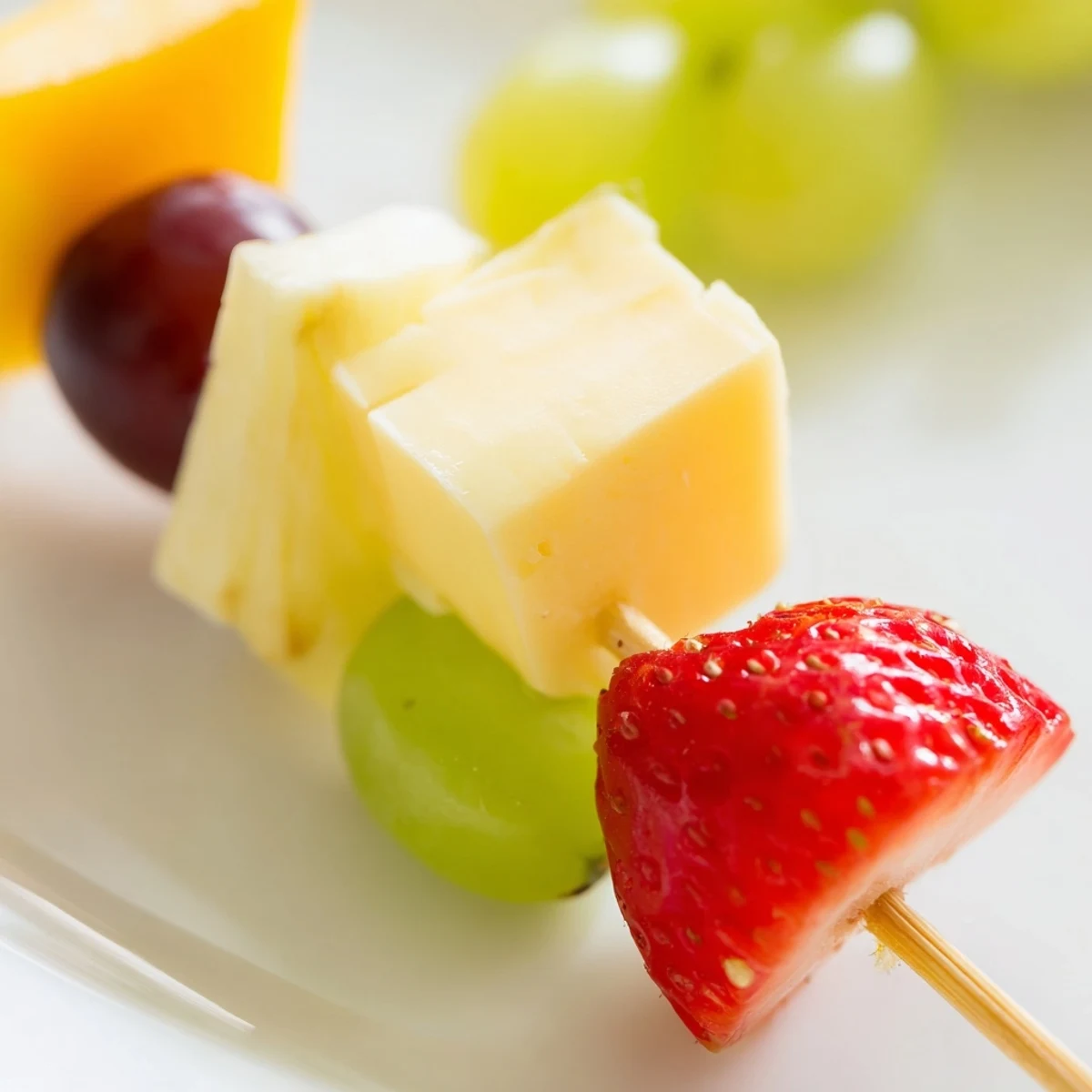 Colorful fruit and cheese kabobs arranged on a platter with grapes, strawberries, pineapple, and cheddar cubes
